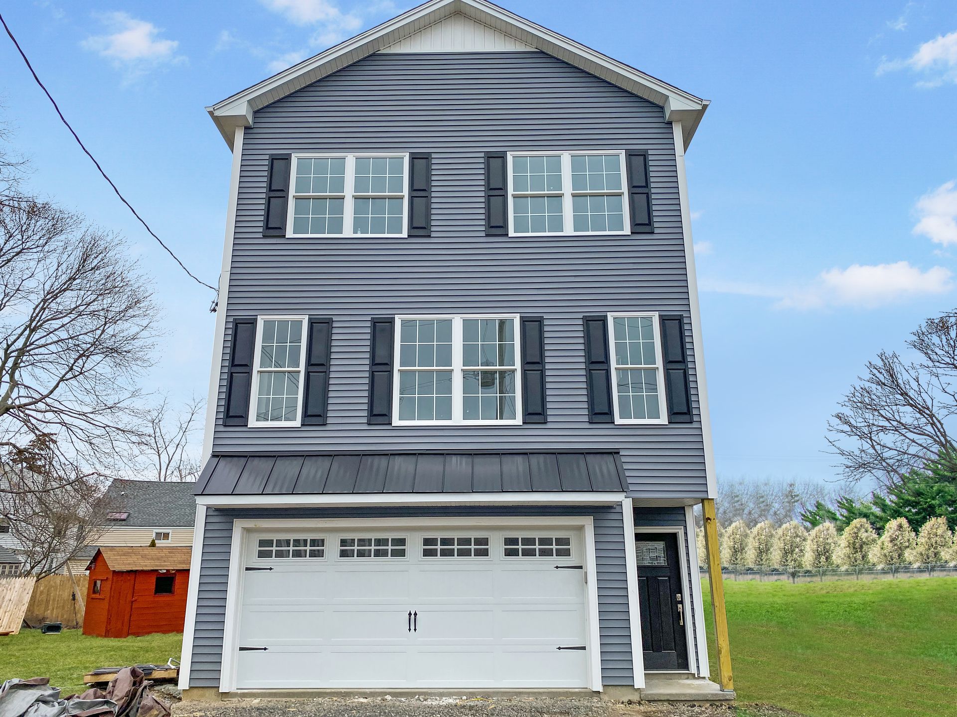 Three-story house with gray siding, white garage door, black shutters, and a small front yard.