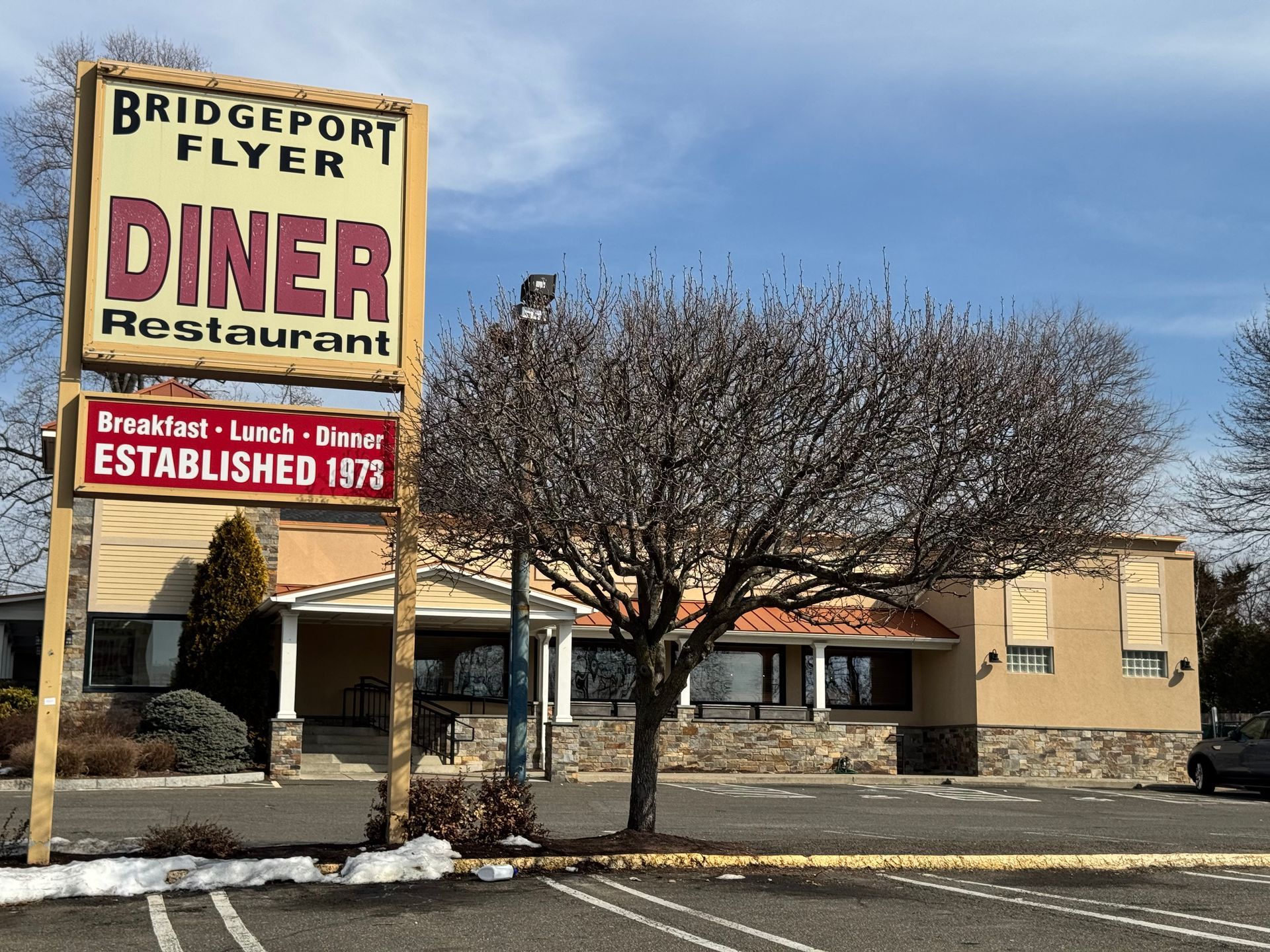 Bridgeport Flyer Diner with sign; tan building, bare tree, blue sky.