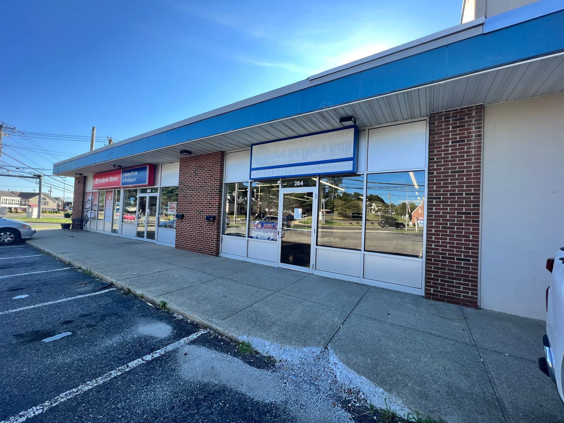 Shops in a strip mall with signs, windows, and a parking lot on a sunny day.