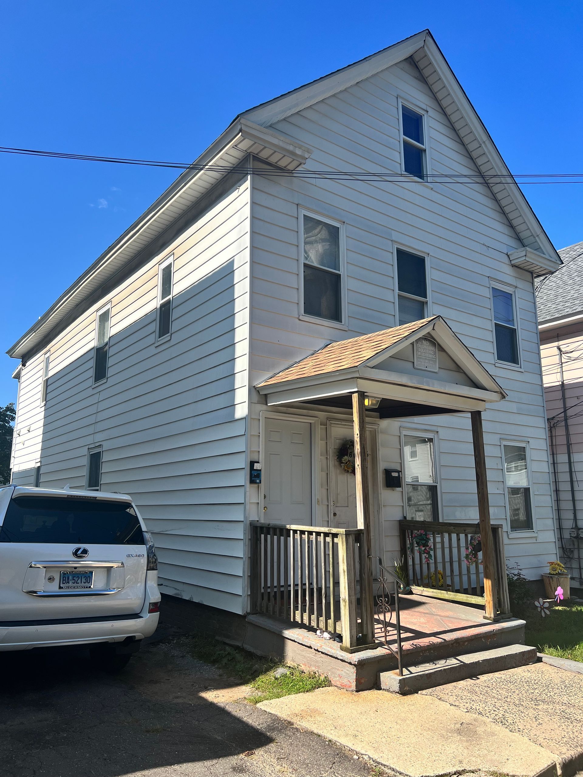 White multi-story house with porch; white car parked in front.