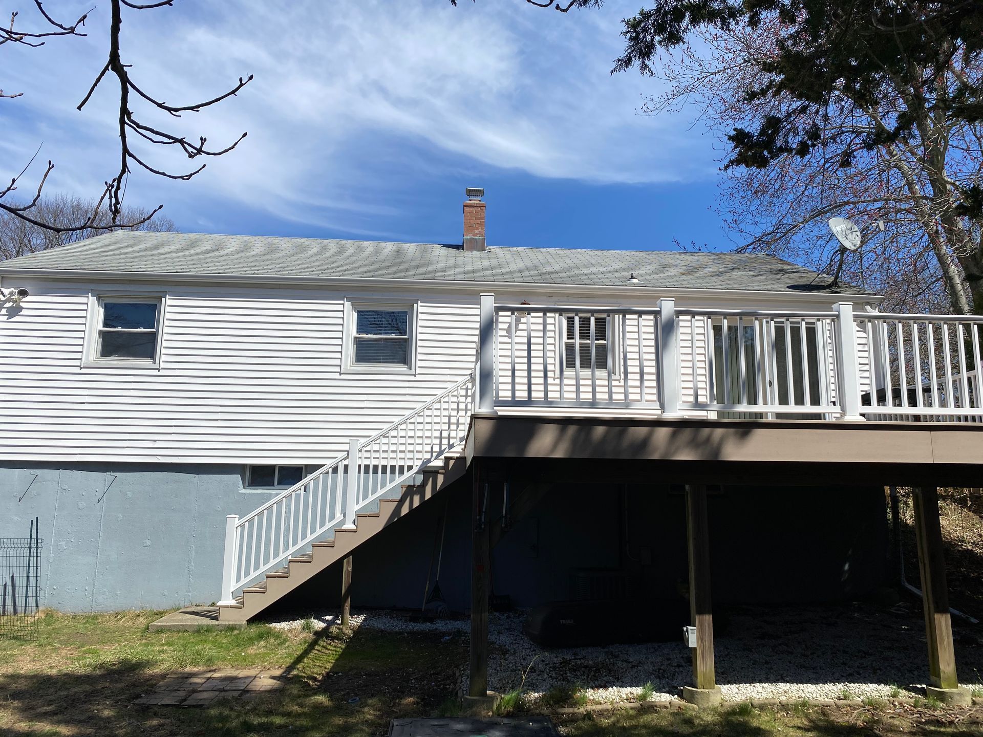 White house with gray roof and deck, stairs leading up to it, blue sky.