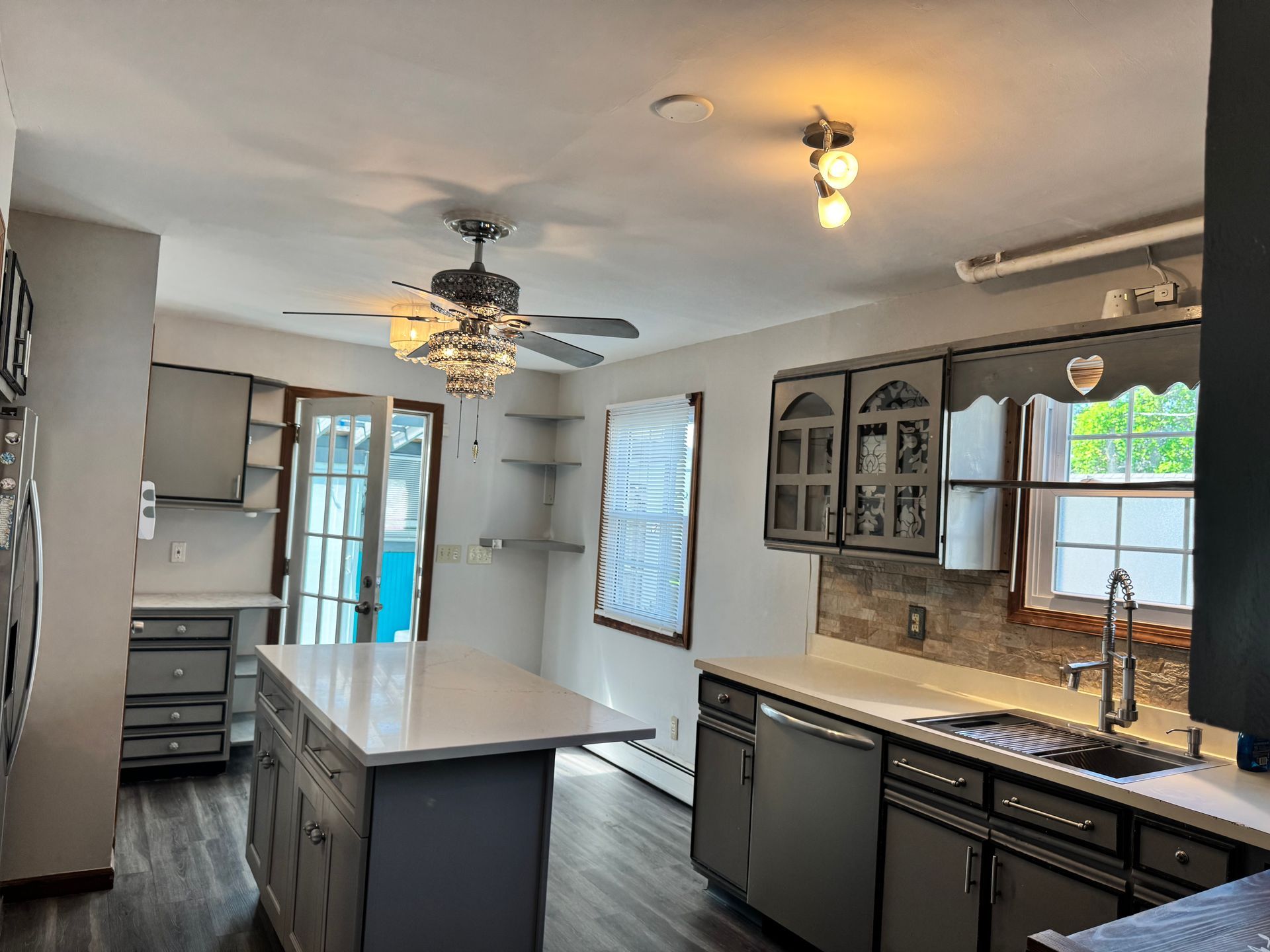 Kitchen with gray cabinets, white countertops, island, and ceiling fan.