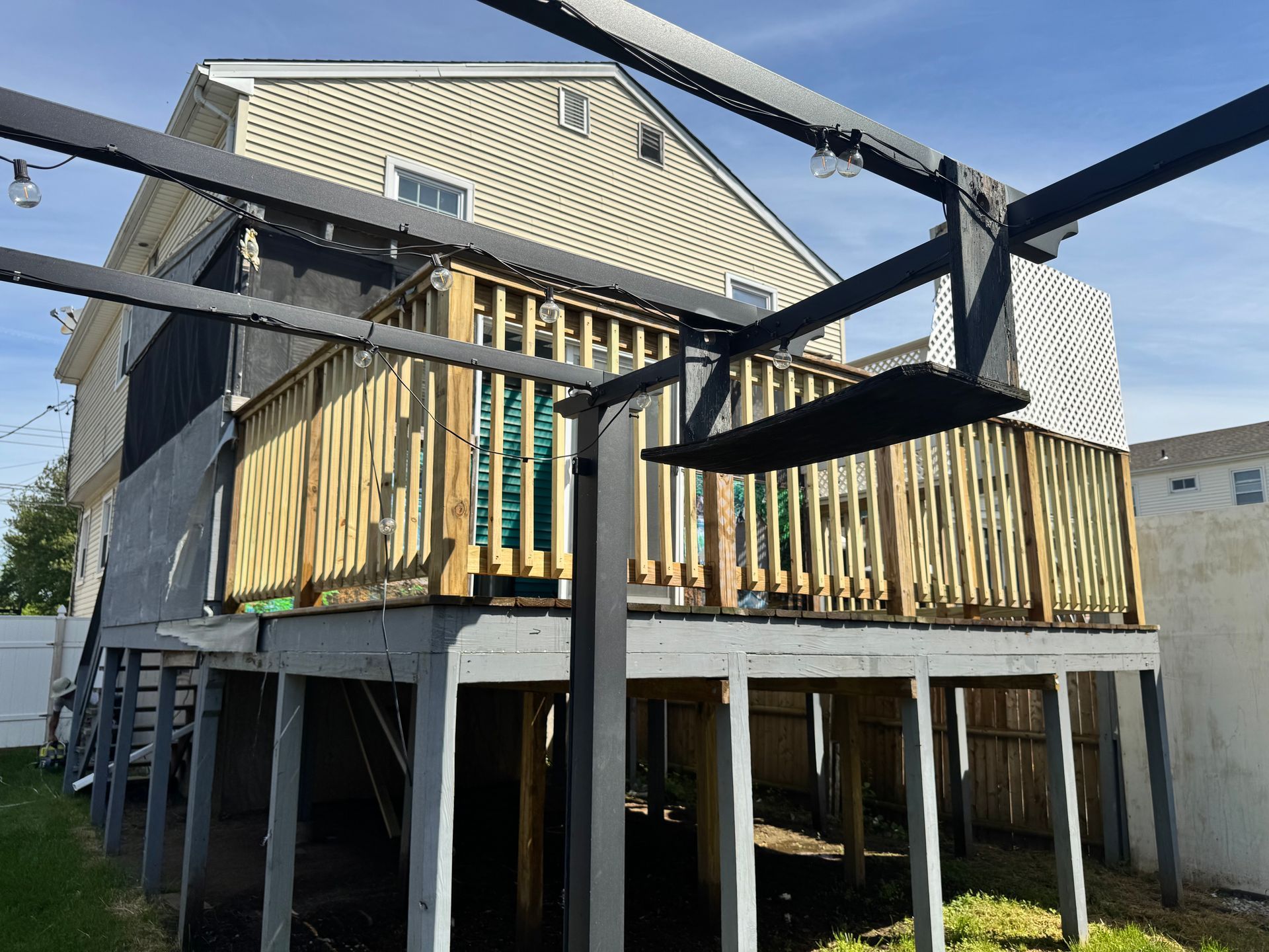 Wooden deck with black pergola attached to a two-story beige house.