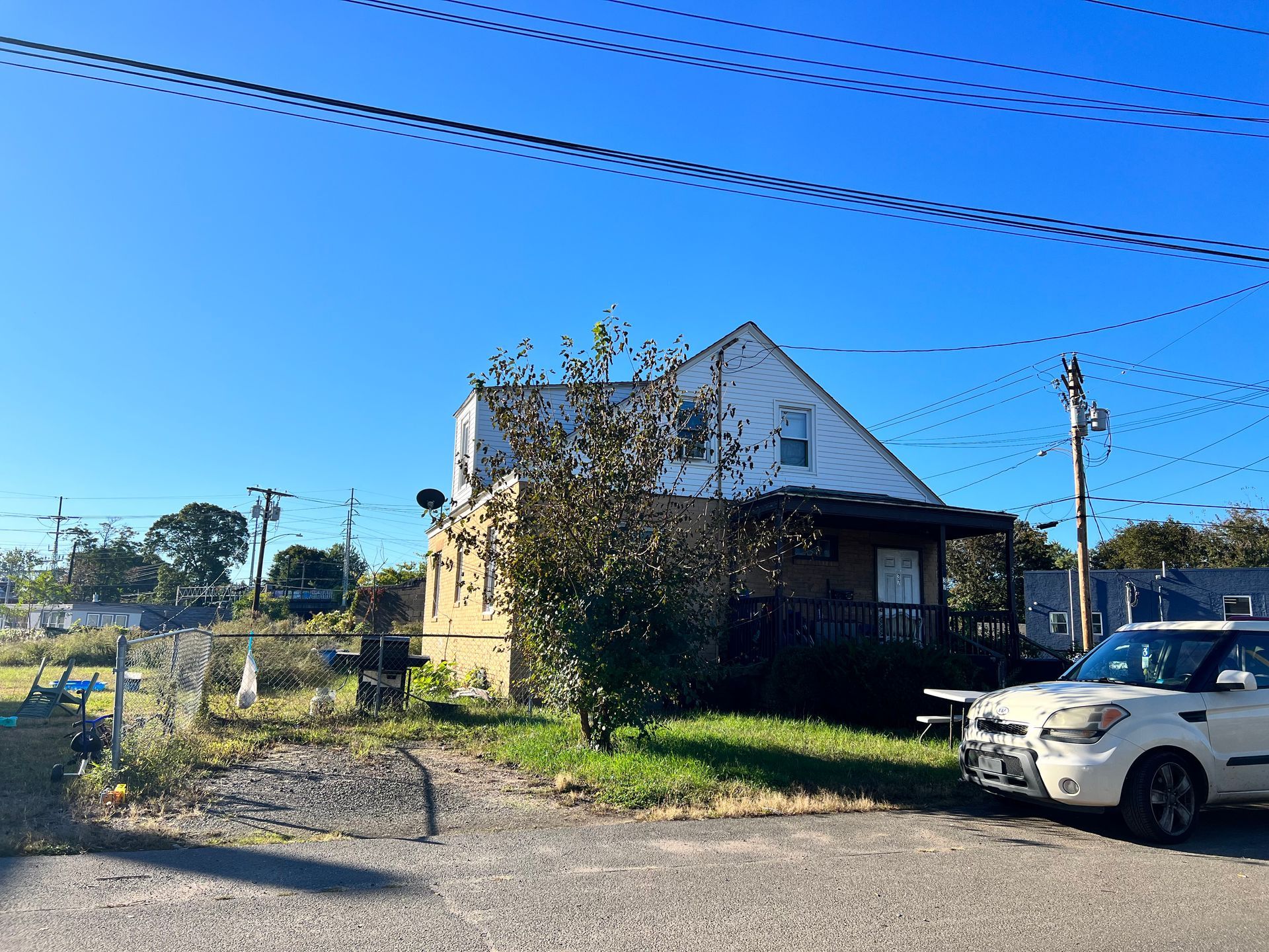 Two-story house with a porch. A white car is parked in front of the house, on a sunny day.