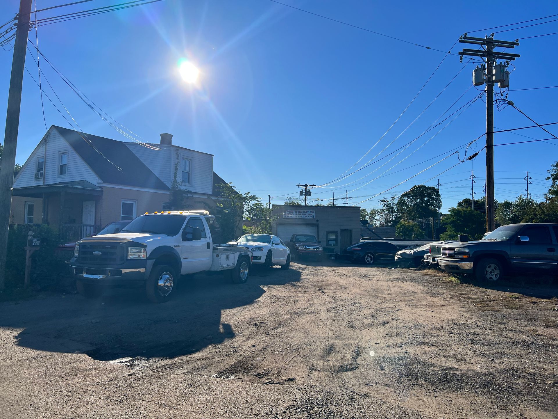 Tow truck in a gravel lot on a sunny day next to a house and auto repair shop.