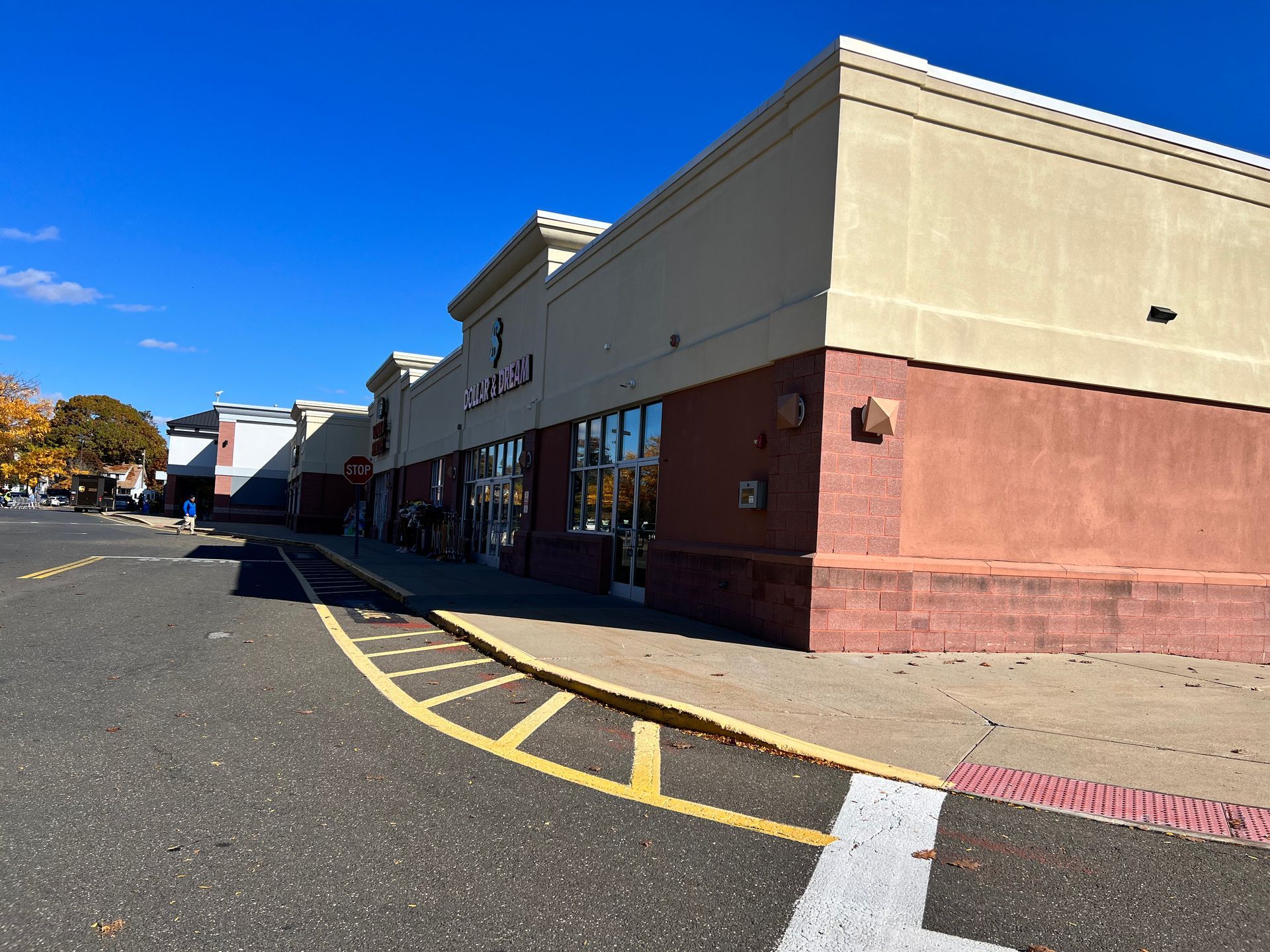 Shopping center exterior on a sunny day. Beige building with red brick base and asphalt parking lot.