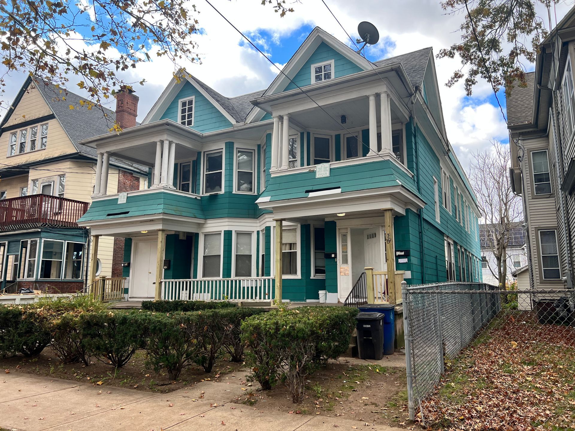 Teal duplex building with white trim and porches, surrounded by foliage, on a street.