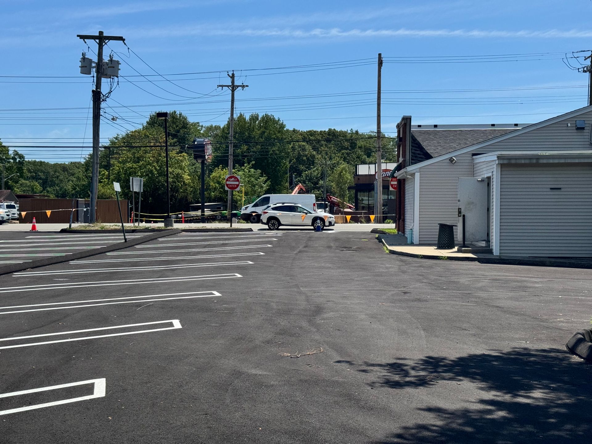 Asphalt parking lot with white lines.  A police car approaches an intersection near some buildings and power lines.