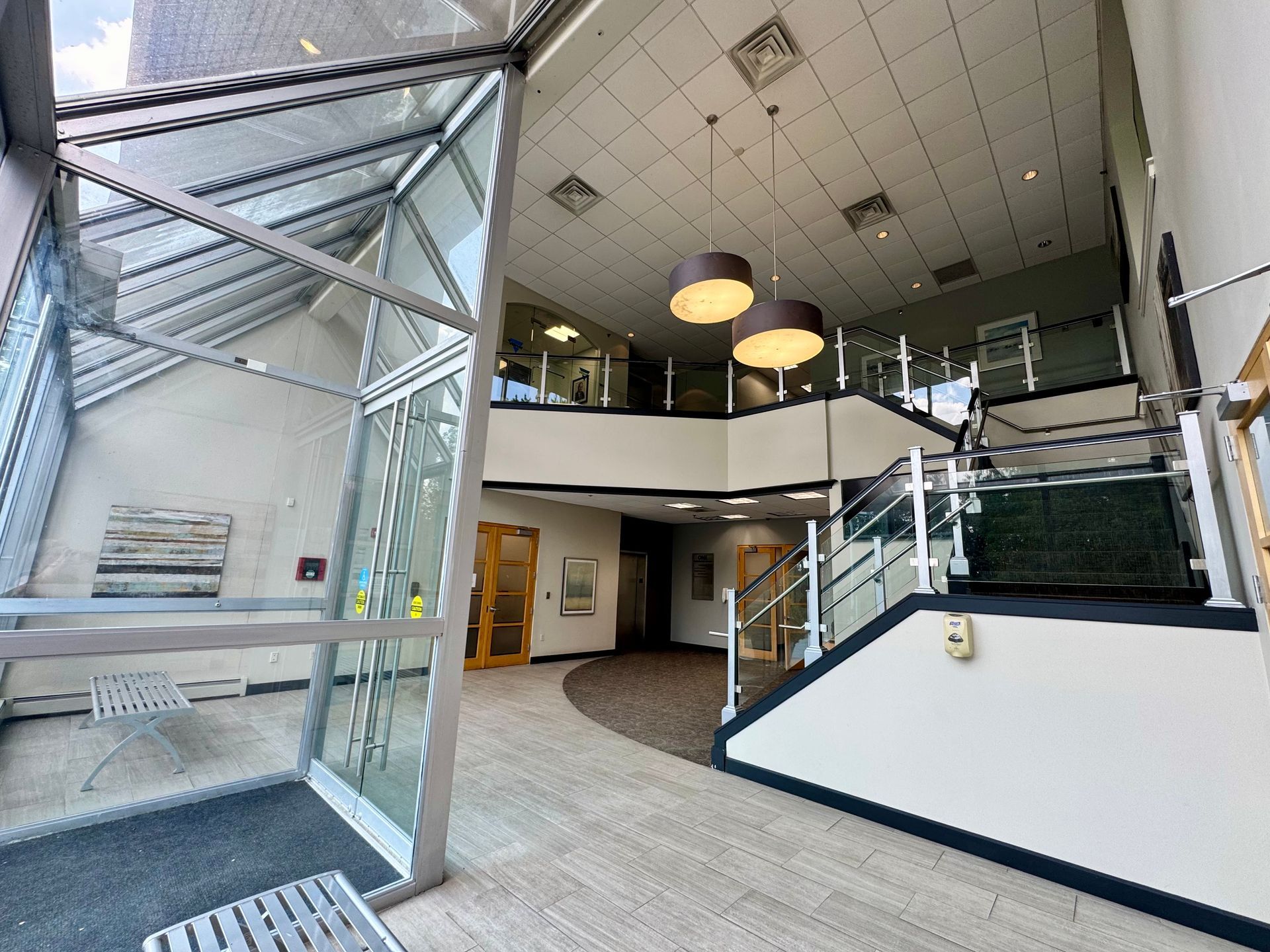 Interior view of a building lobby with glass walls, stairs, and two hanging lights.