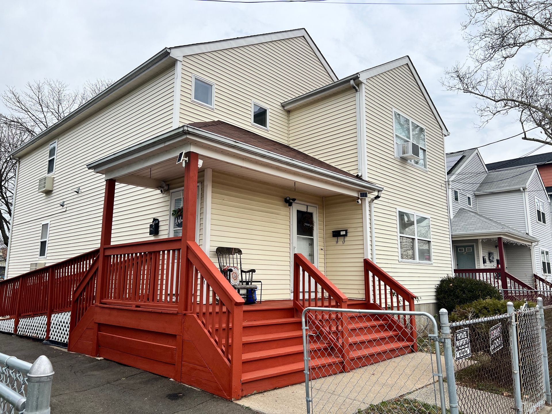 Two-story cream house with a red porch and stairs; a smaller house is to the right.