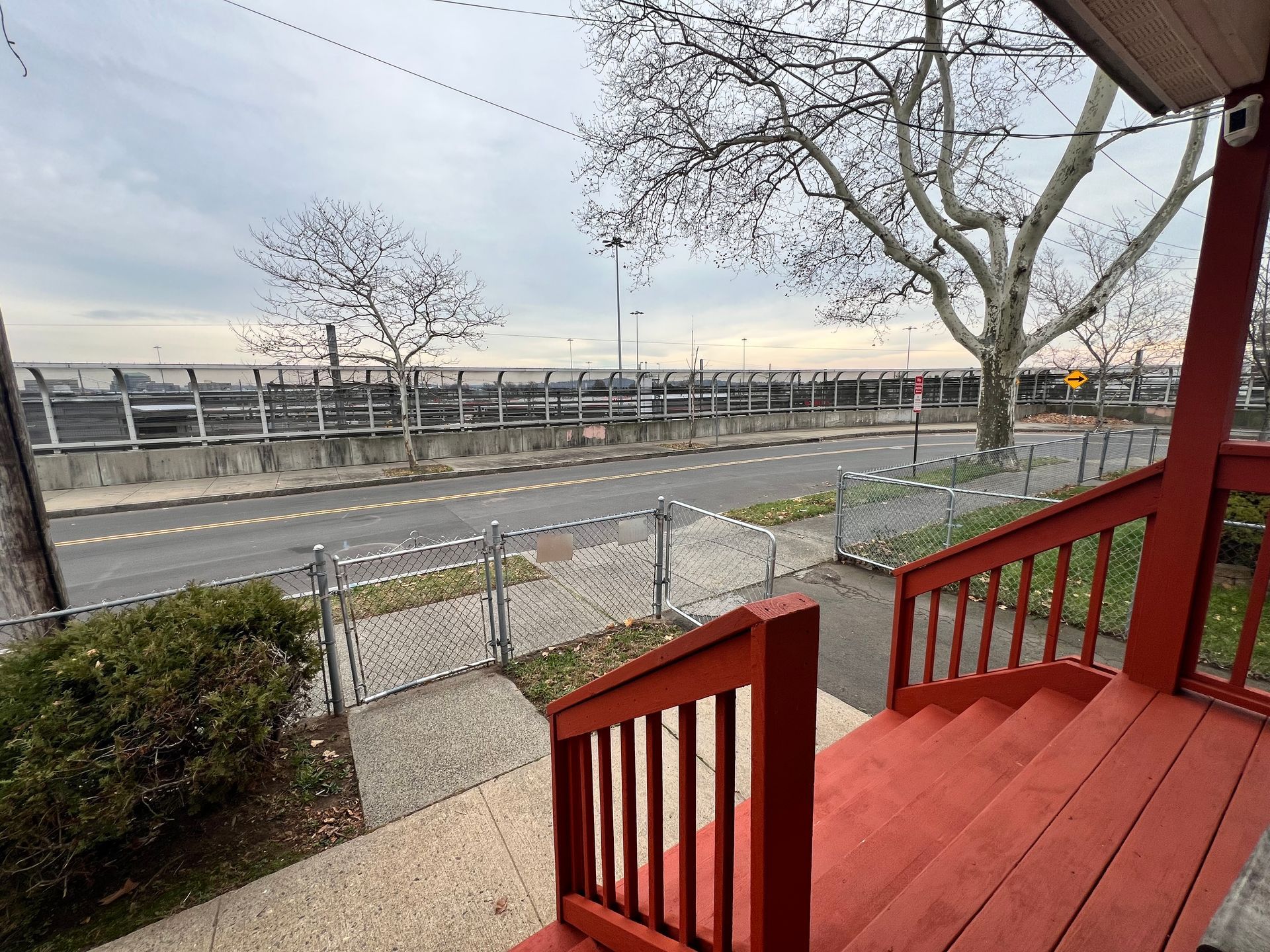 Red stairs lead to a view of a road, a fence, and a bare tree under a cloudy sky.