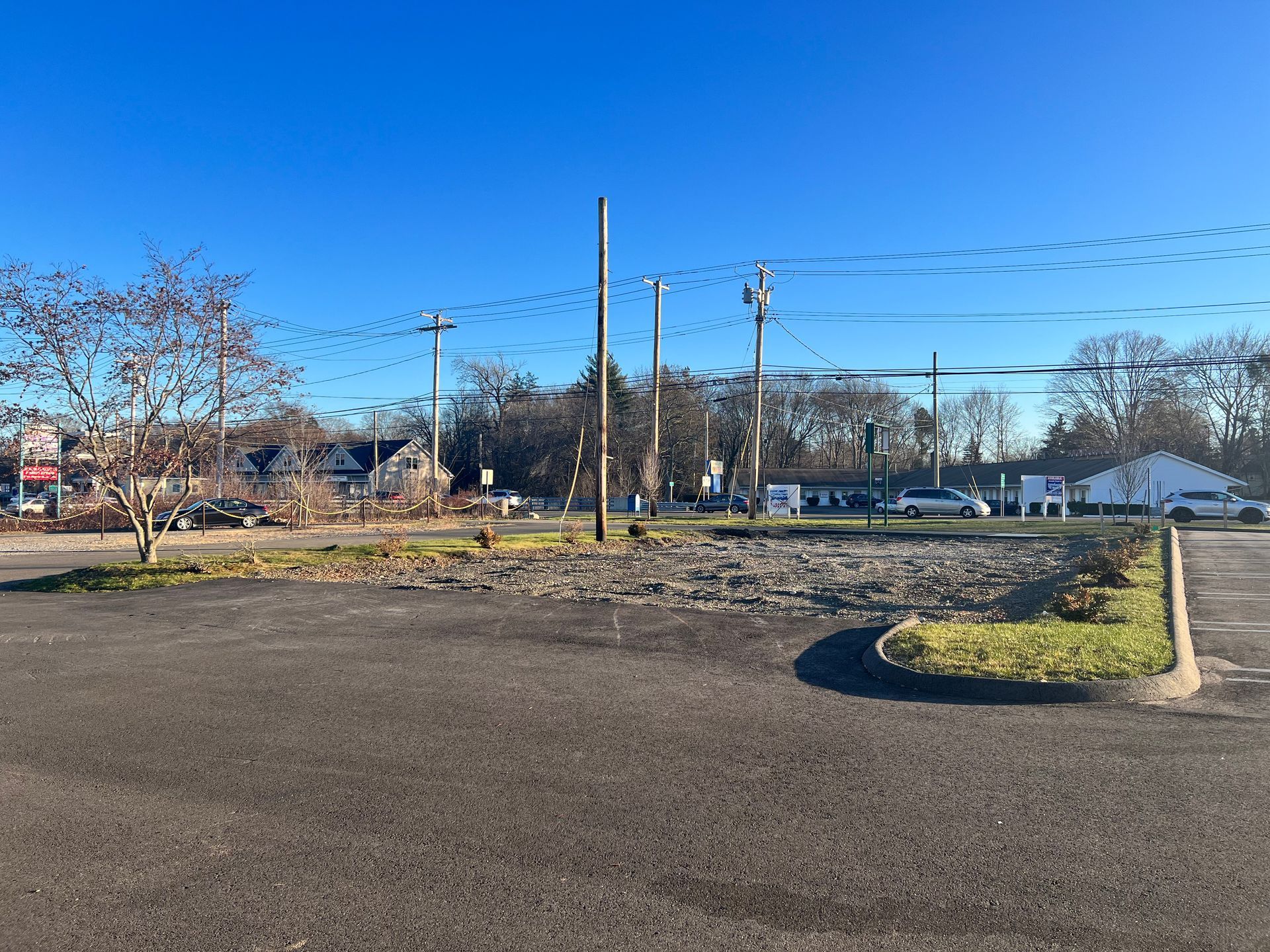 Open asphalt parking lot with utility poles and power lines under a clear, blue sky.