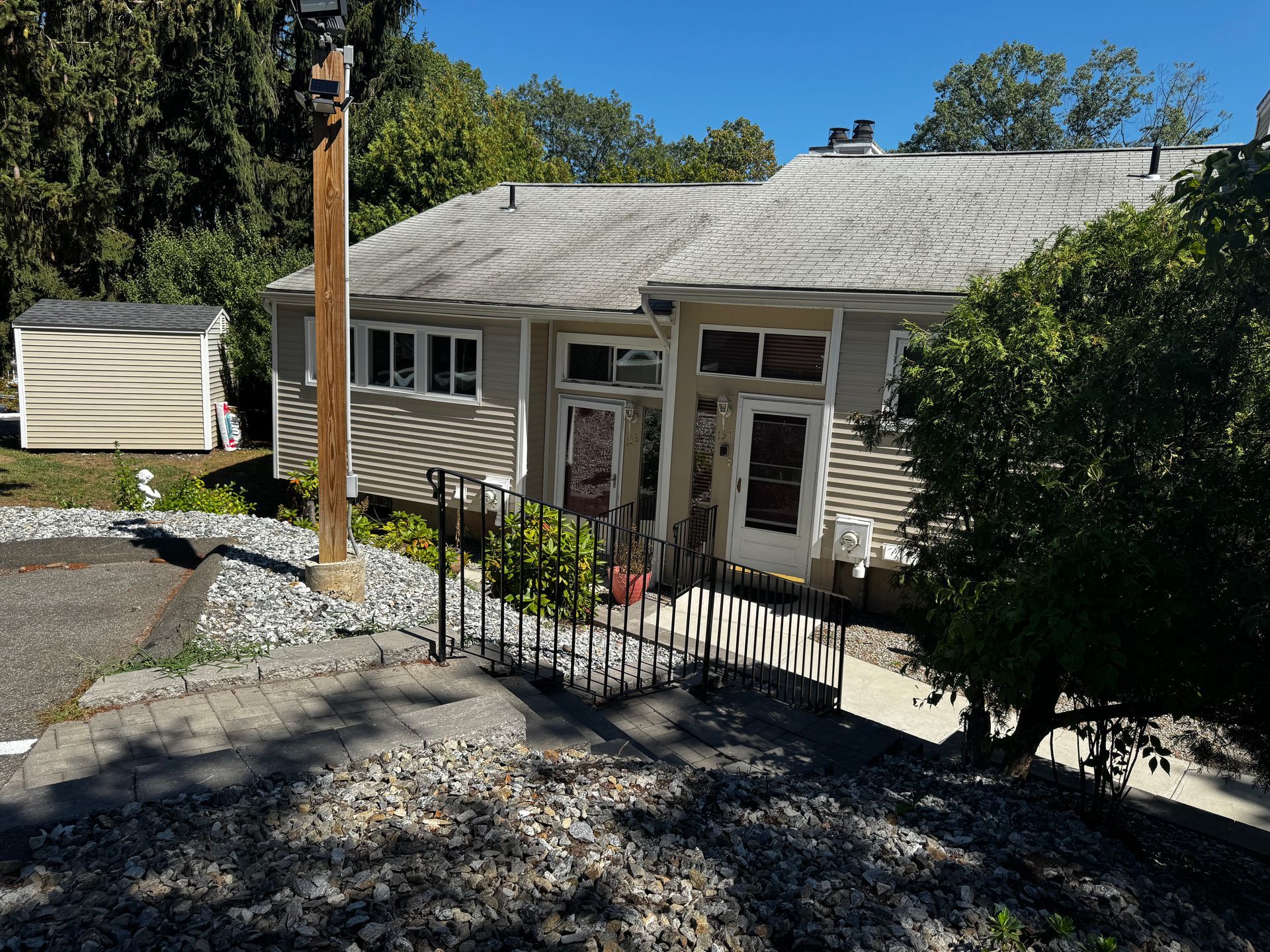 Gray house with a dark fence. Trees and a utility pole are visible. Sunny day.