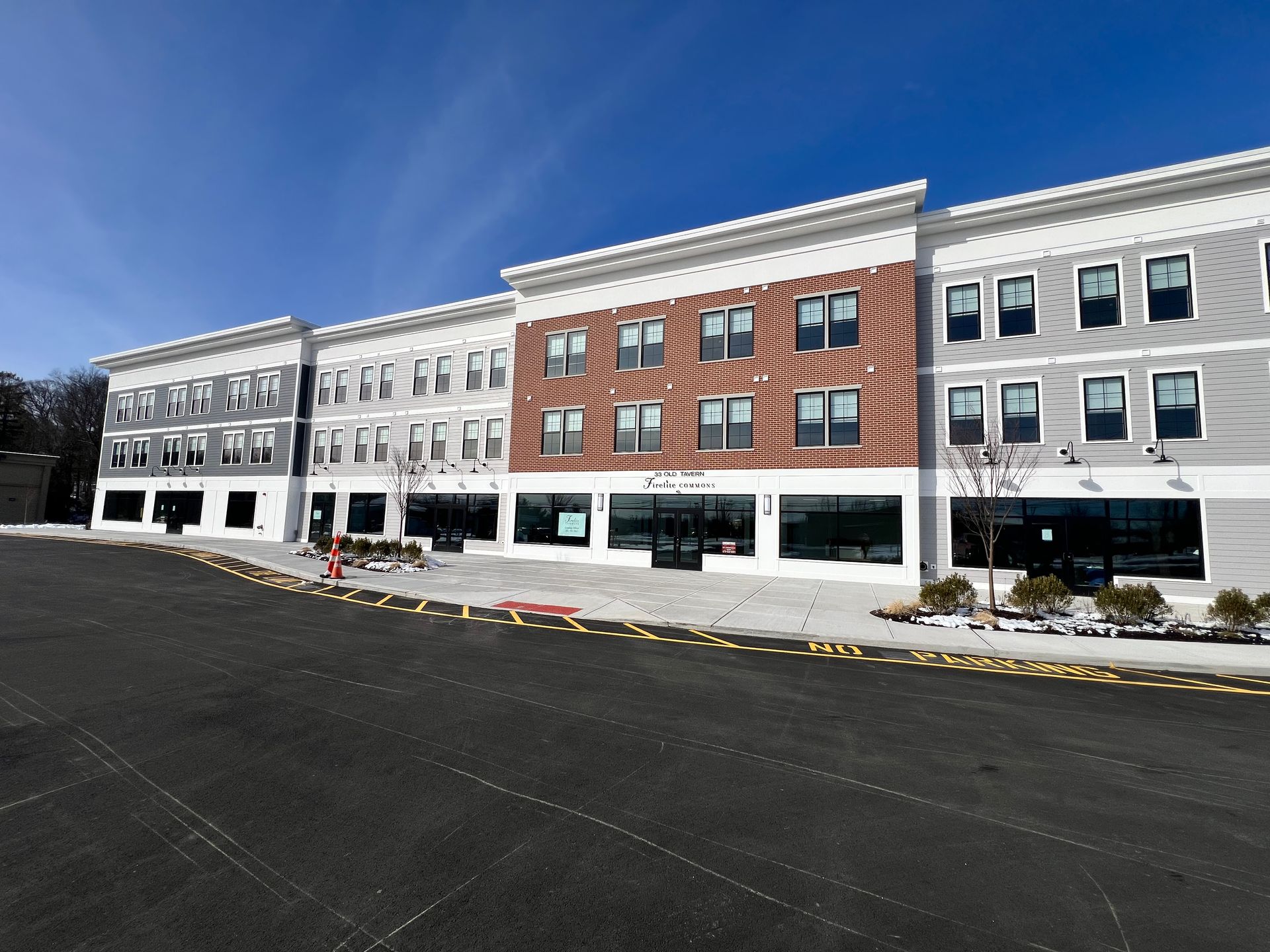 Multi-story commercial building with grey, white and red brick facade. Black storefront windows. Blue sky.