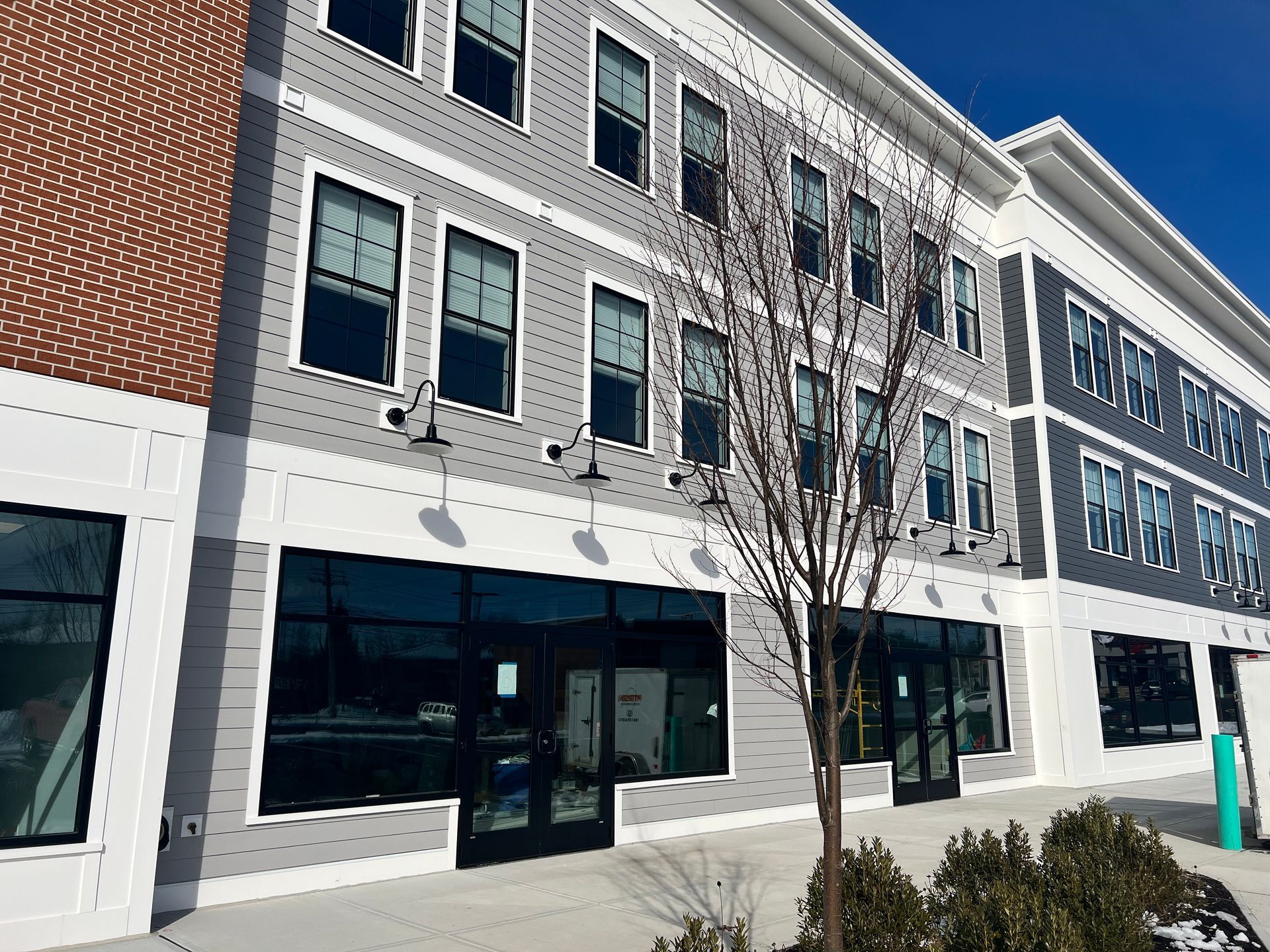 Multi-story building with storefronts on the ground level and gray siding above, under a blue sky.