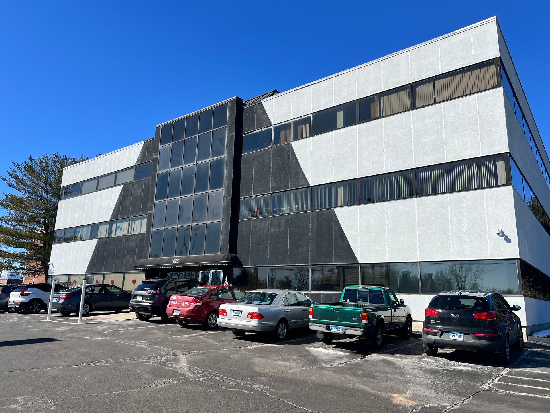 Office building with black and white facade, parked cars in front, and blue sky.