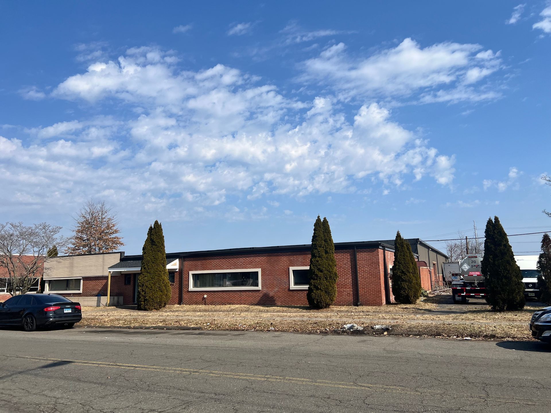 A low, brown building with windows and evergreens against a blue sky with clouds.