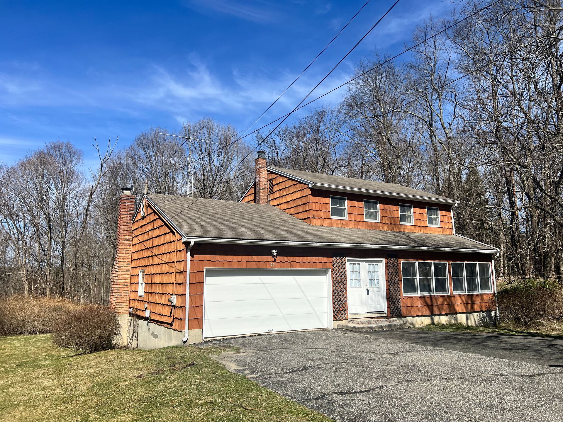 Two-story brick house with a white garage door, trees in the background, and a blue sky.