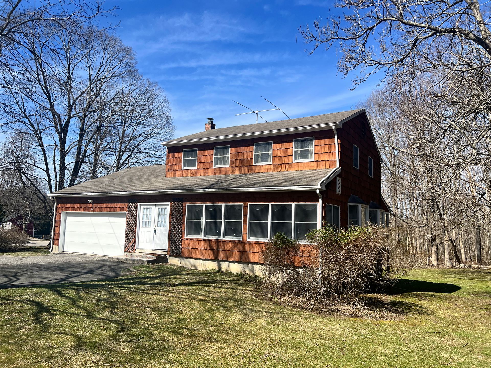 Two-story brown house with attached garage, windows across the front, set in a grassy yard under a blue sky.