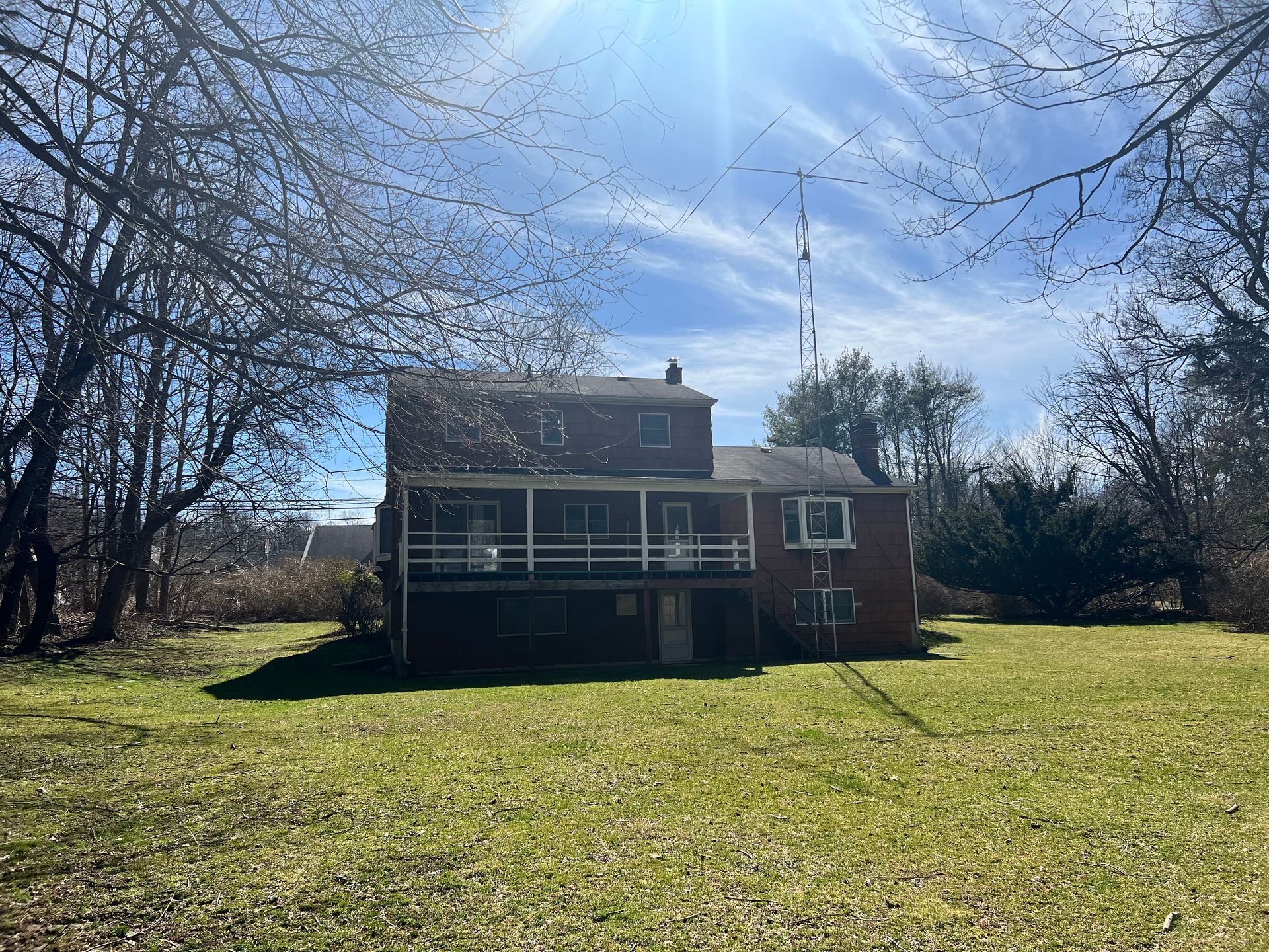 Back view of a two-story brick house with a covered porch and bare trees against a blue sky.