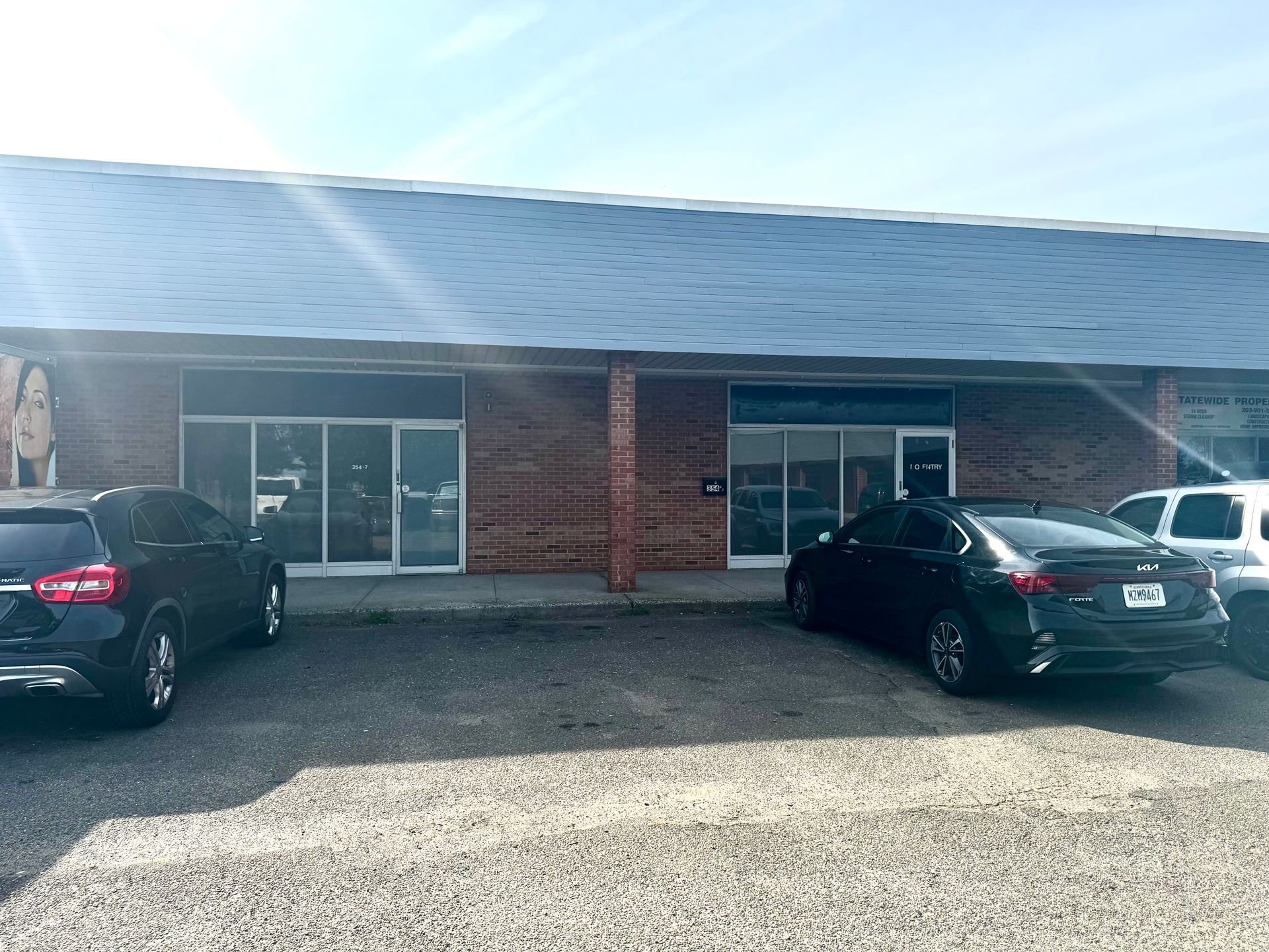 Exterior view of a brick building with glass doors and parked cars in front; blue sky overhead.