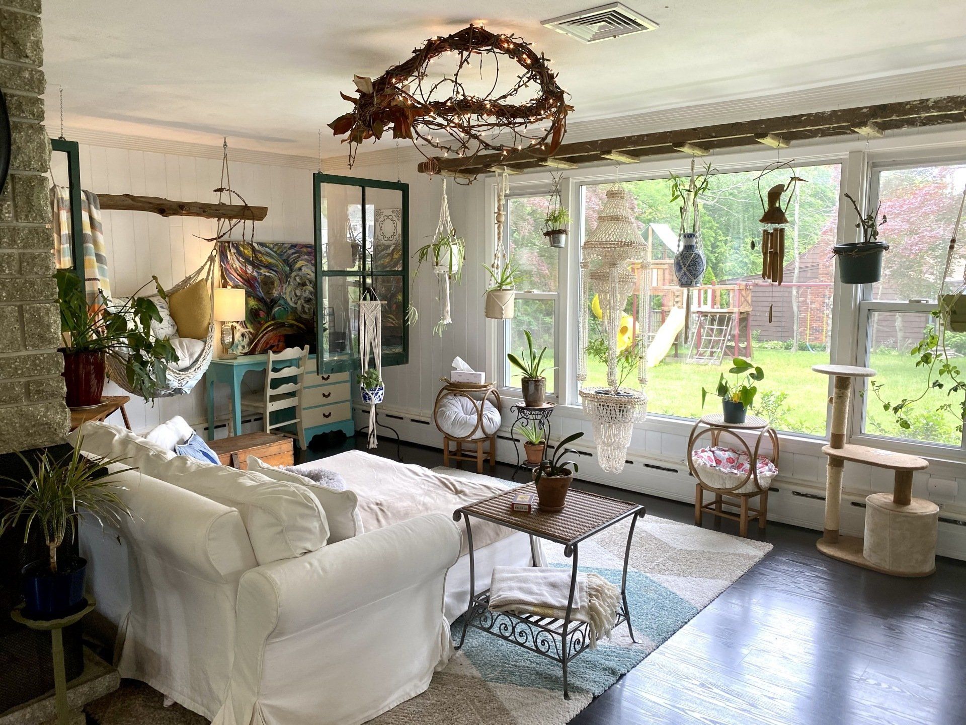 Bright sunlit living room with plants, white sofa, vintage decor, and a view of the outdoors.
