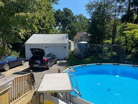 Backyard with pool, cars in driveway, garage, boat, and trees on a sunny day.