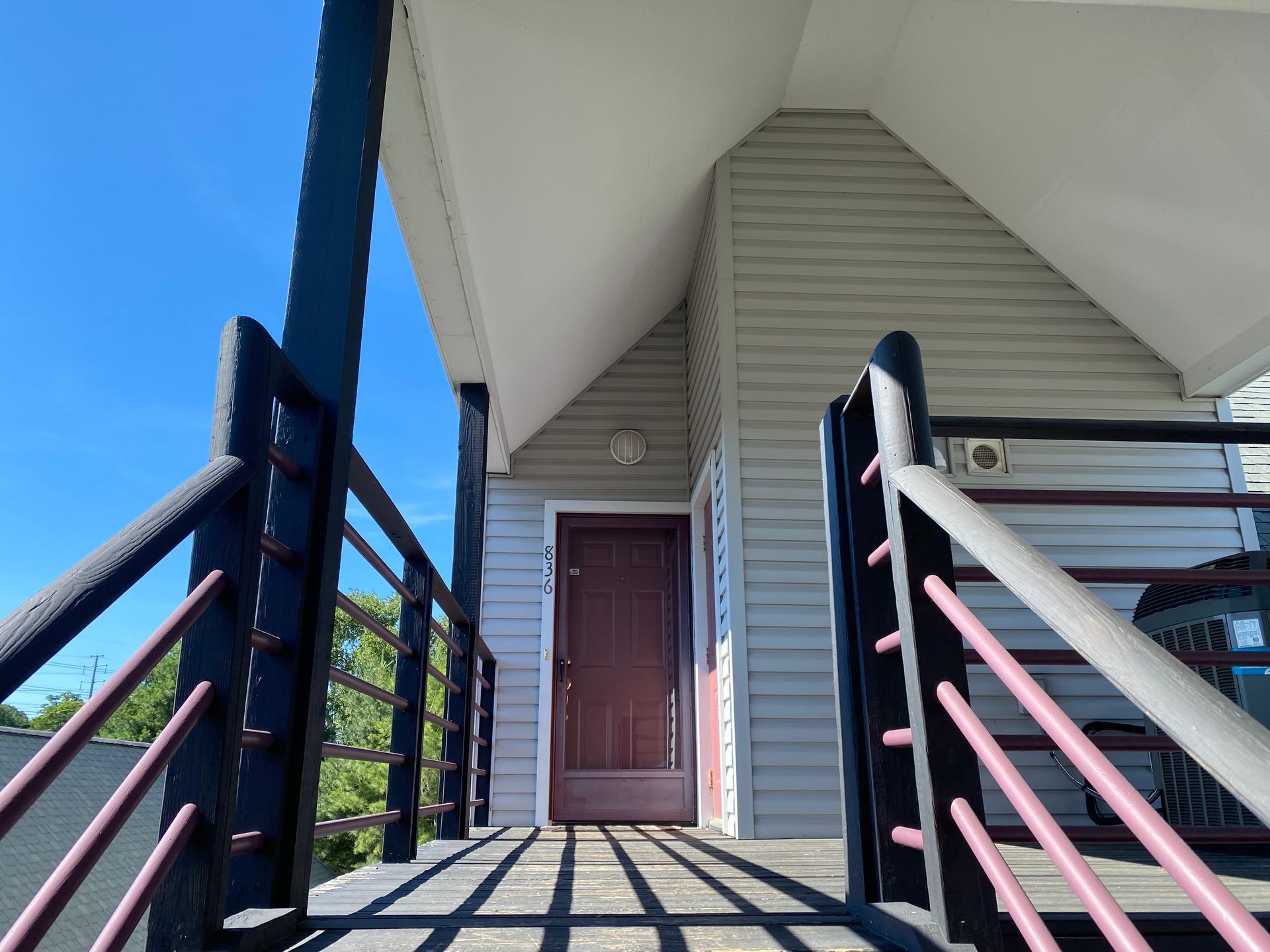 Wooden deck leading to a brown door under a white peaked roof. Black railings on either side.