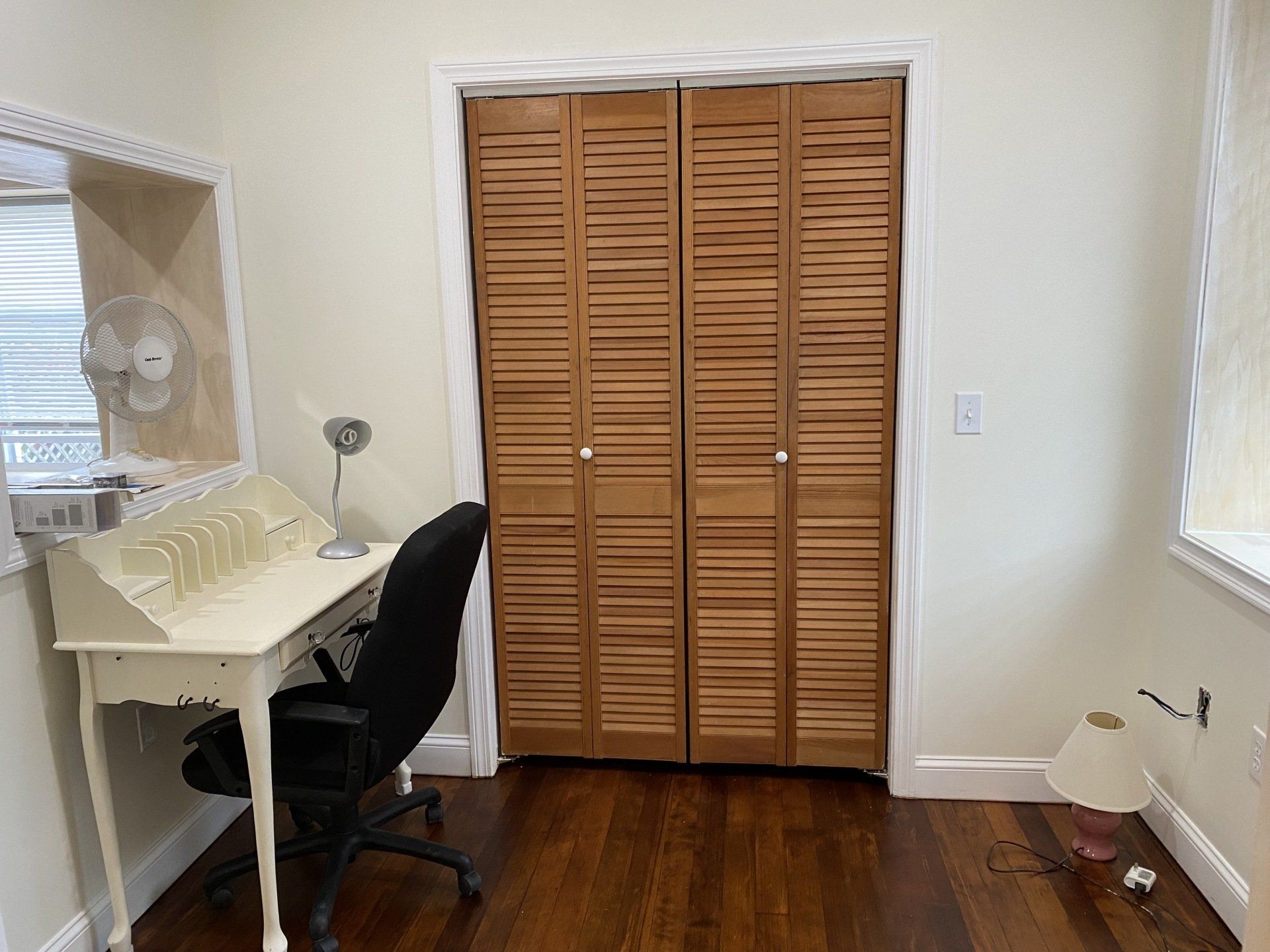 A room with a closet, desk, mirror, and a lamp on the floor.