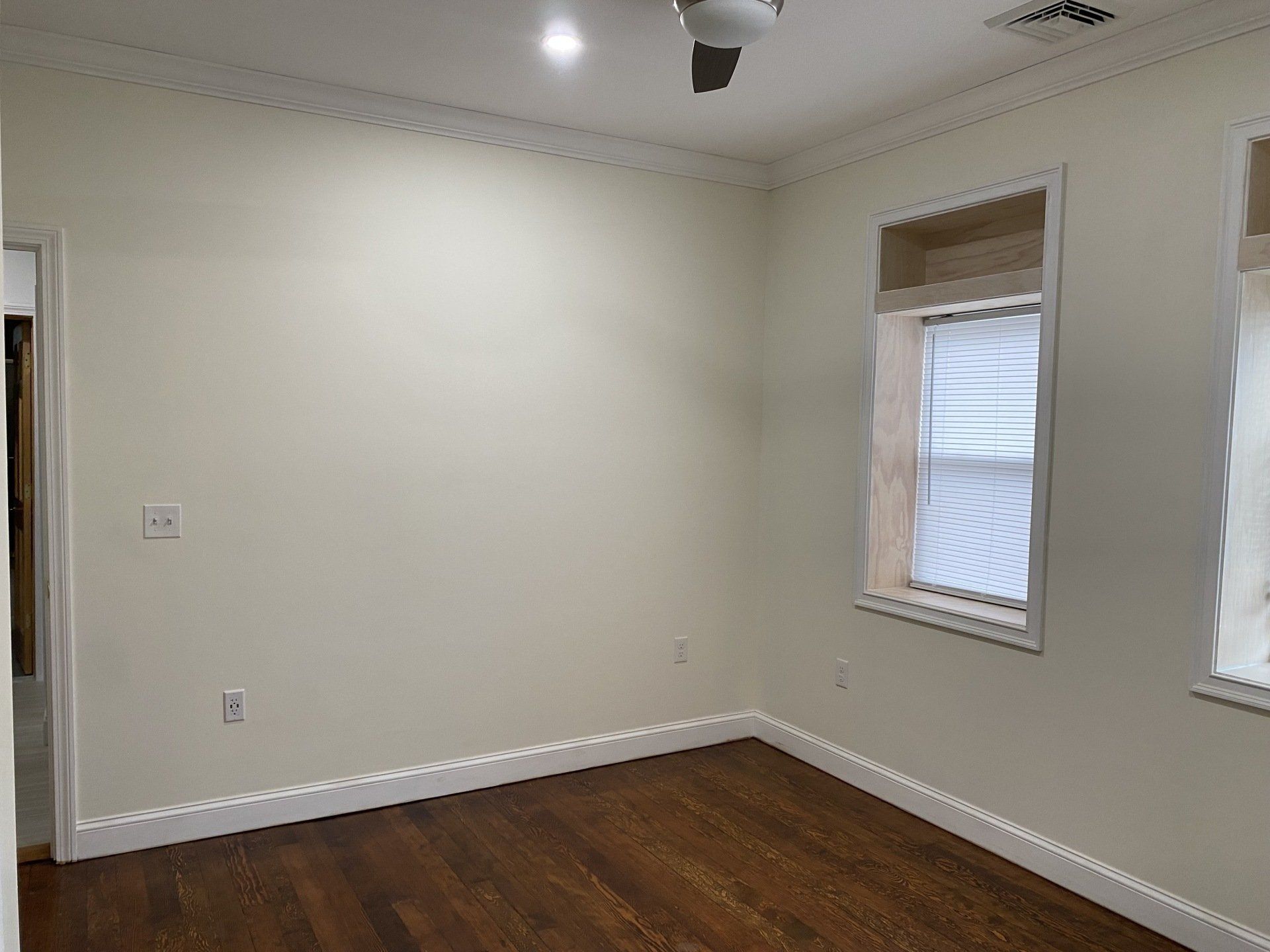 Empty room with dark wood floor, light walls, and two windows.