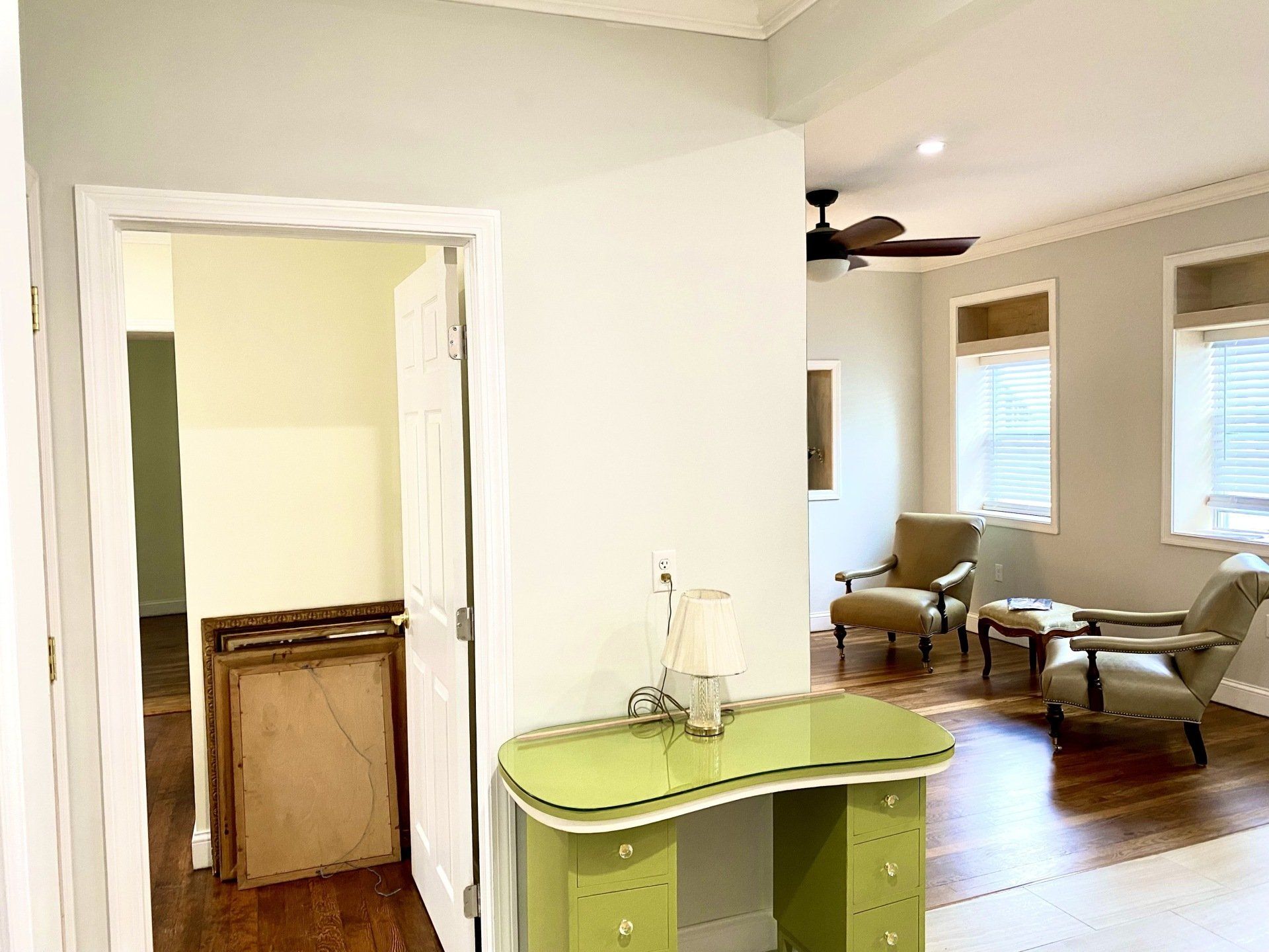 Green desk in front of a doorway leading to a room with seating, windows, and a ceiling fan.