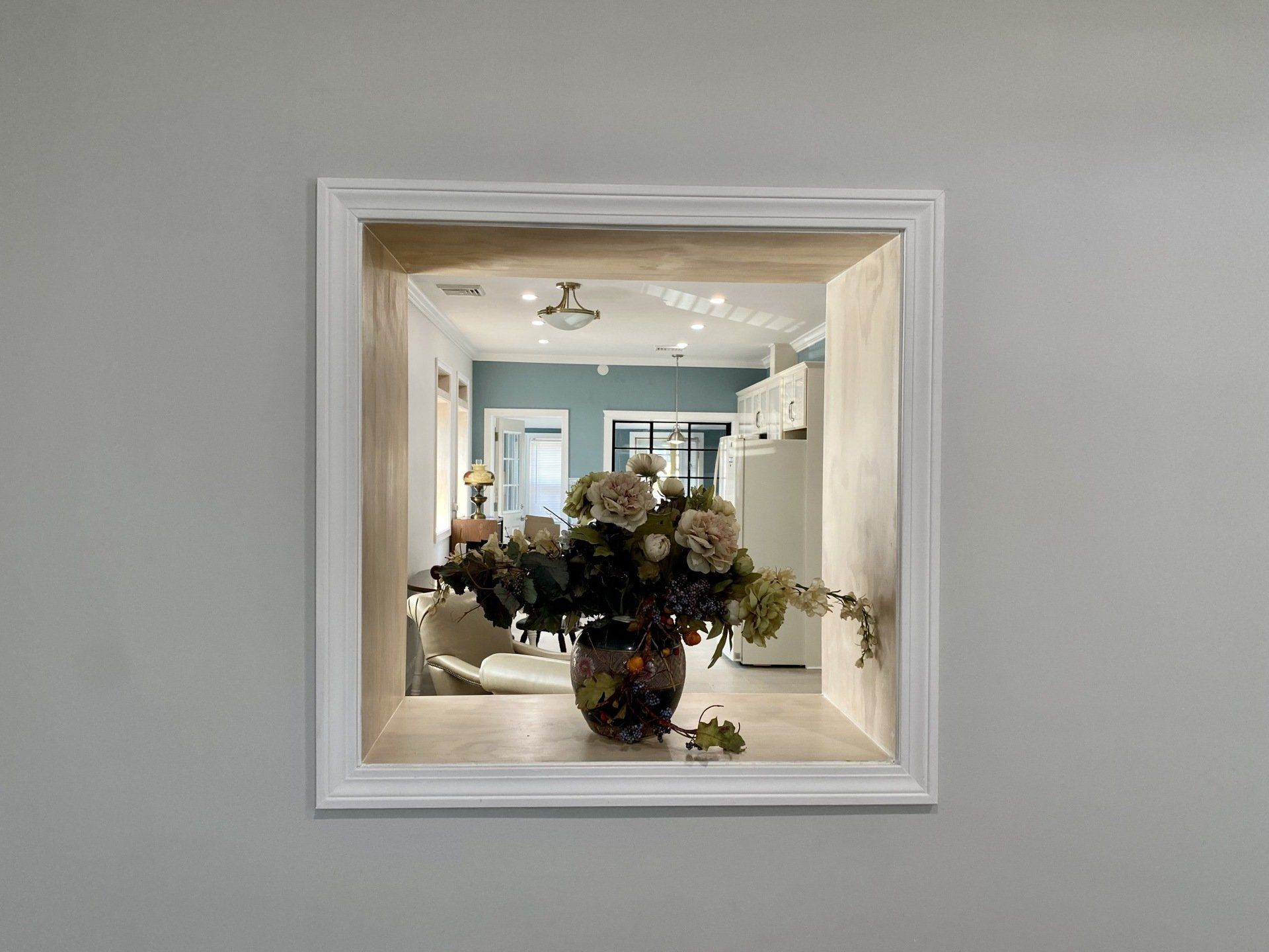 Square mirror recess on gray wall; floral arrangement in a vase; interior view reflected.
