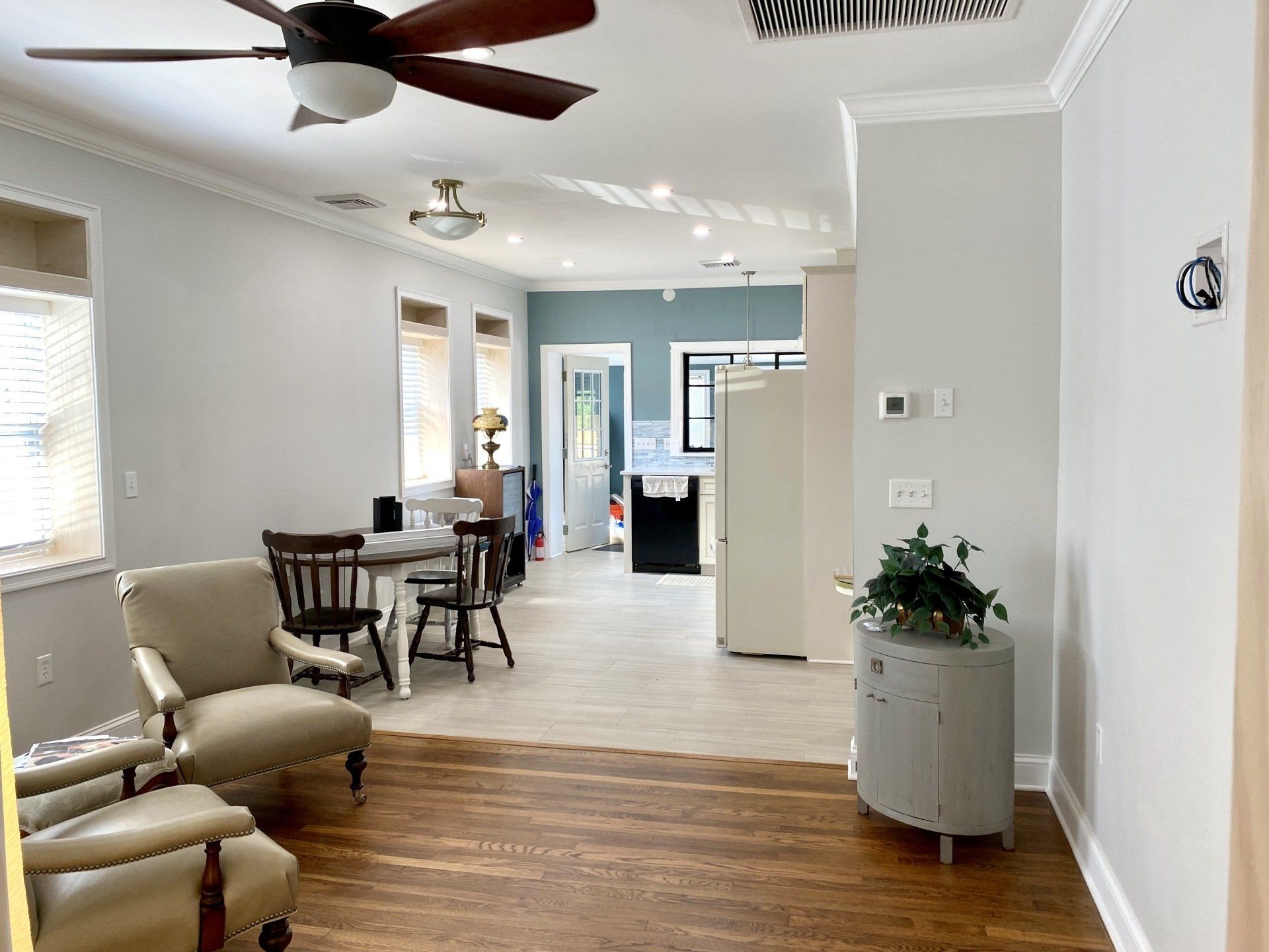 Open-plan living space with dining area, chairs, cabinets, ceiling fans, and a glimpse into the kitchen.