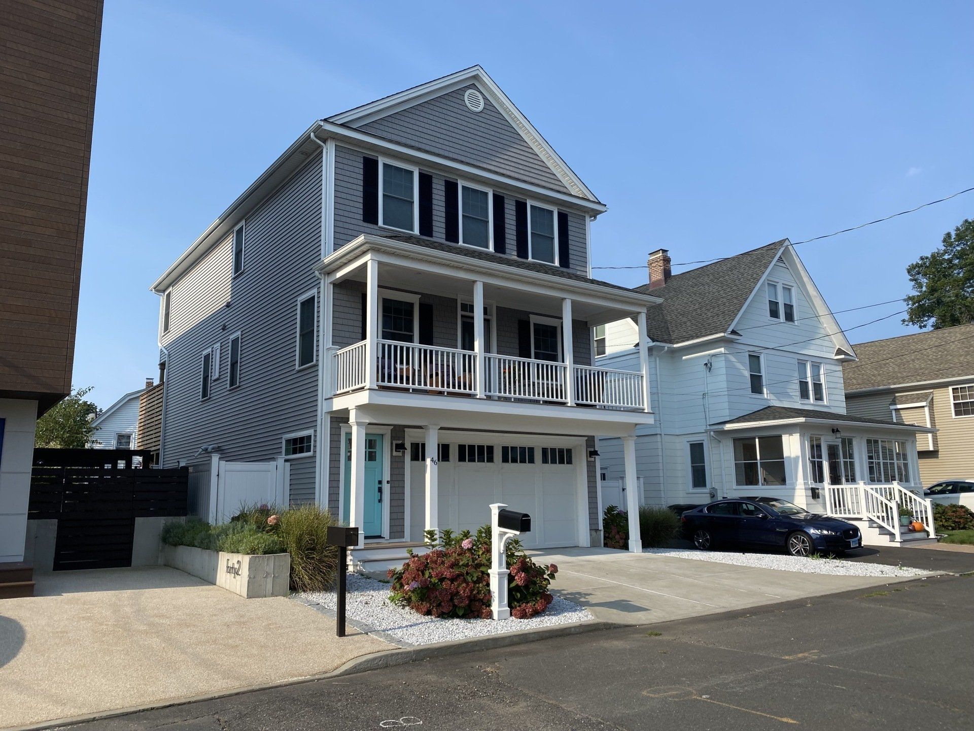 Gray house with white porch and blue door, parked car in driveway.