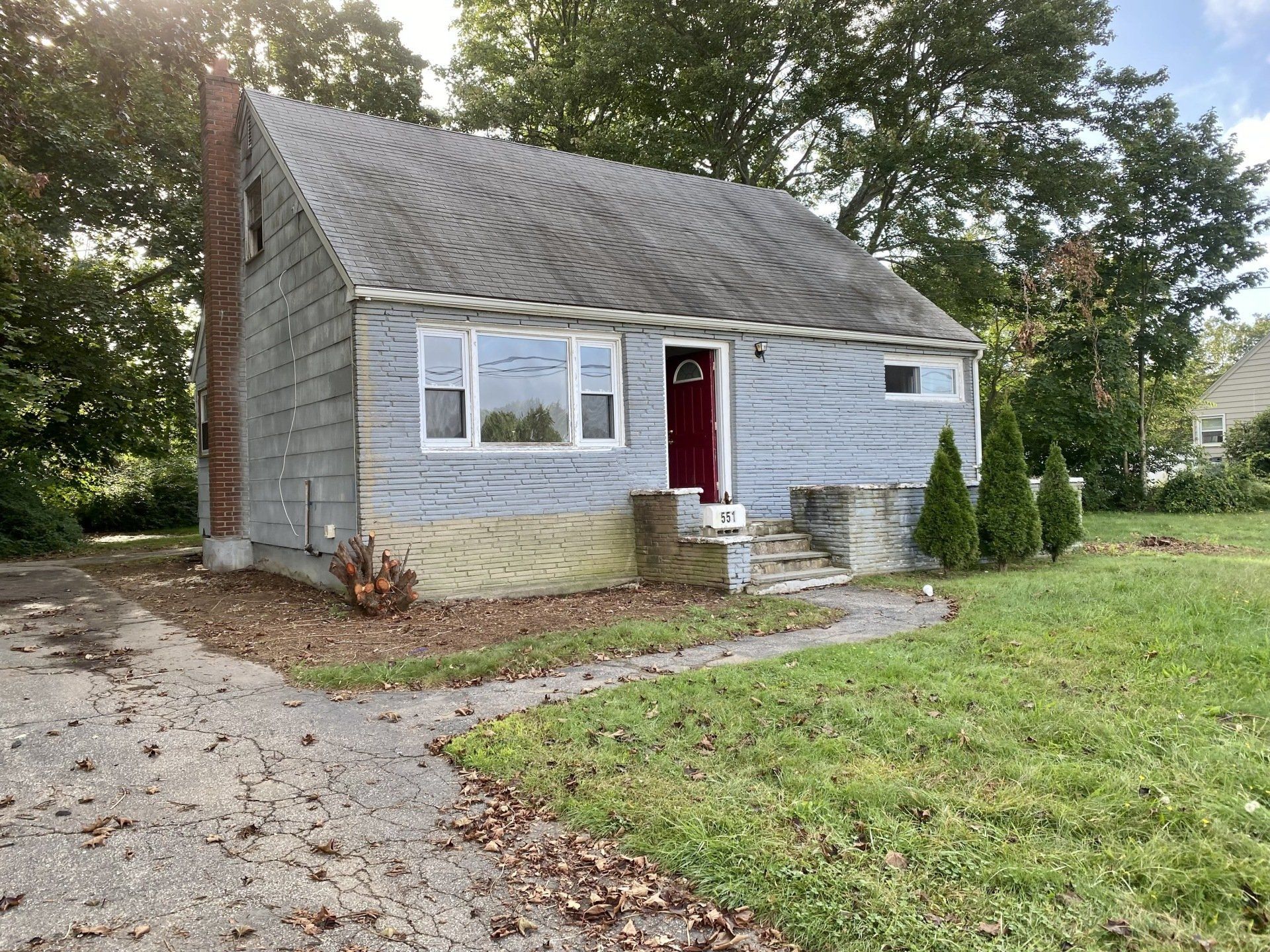A weathered, gray single-story house with a brick chimney and a red front door.