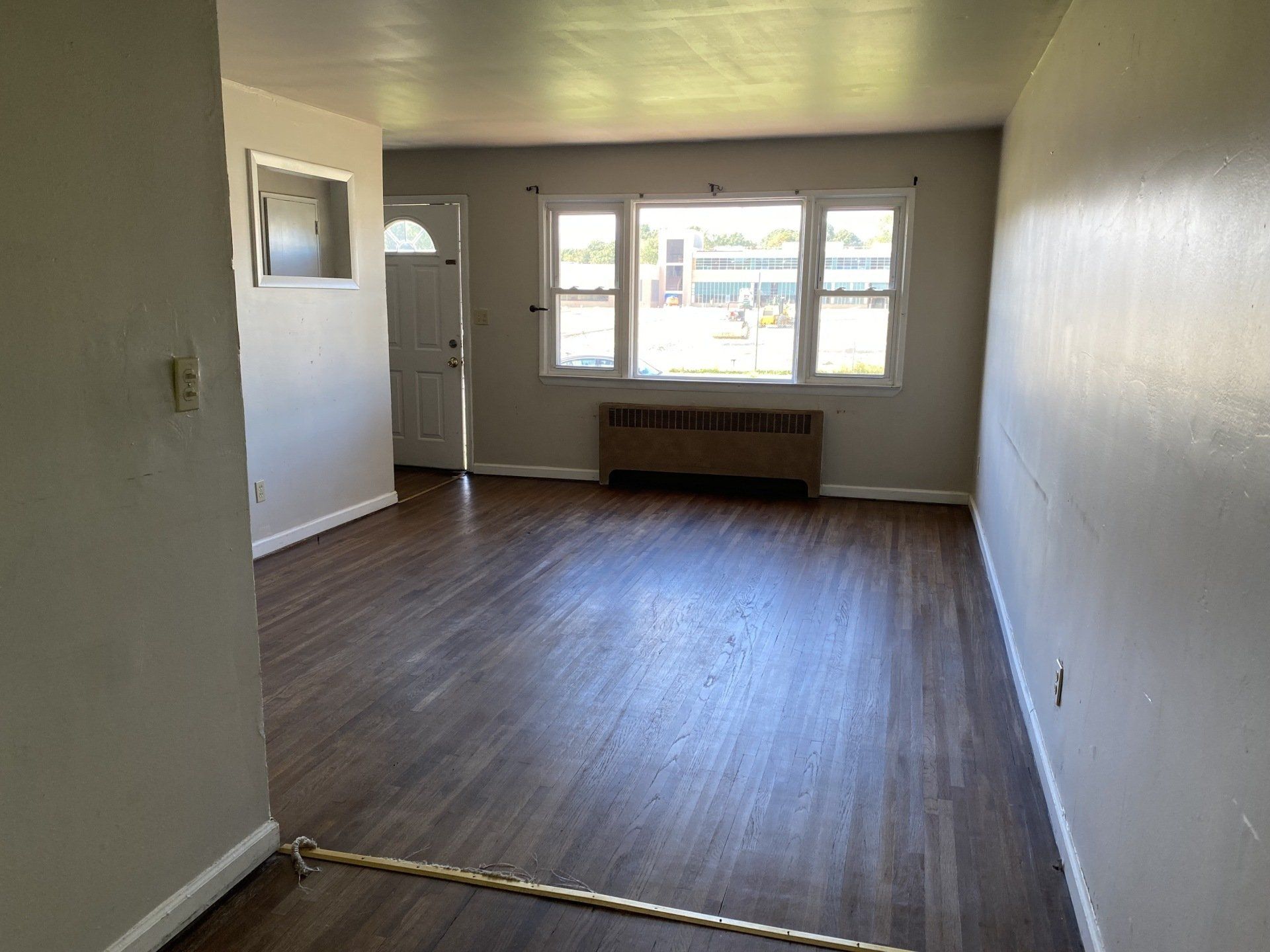 Empty living room with dark wood floors, gray walls, and window.