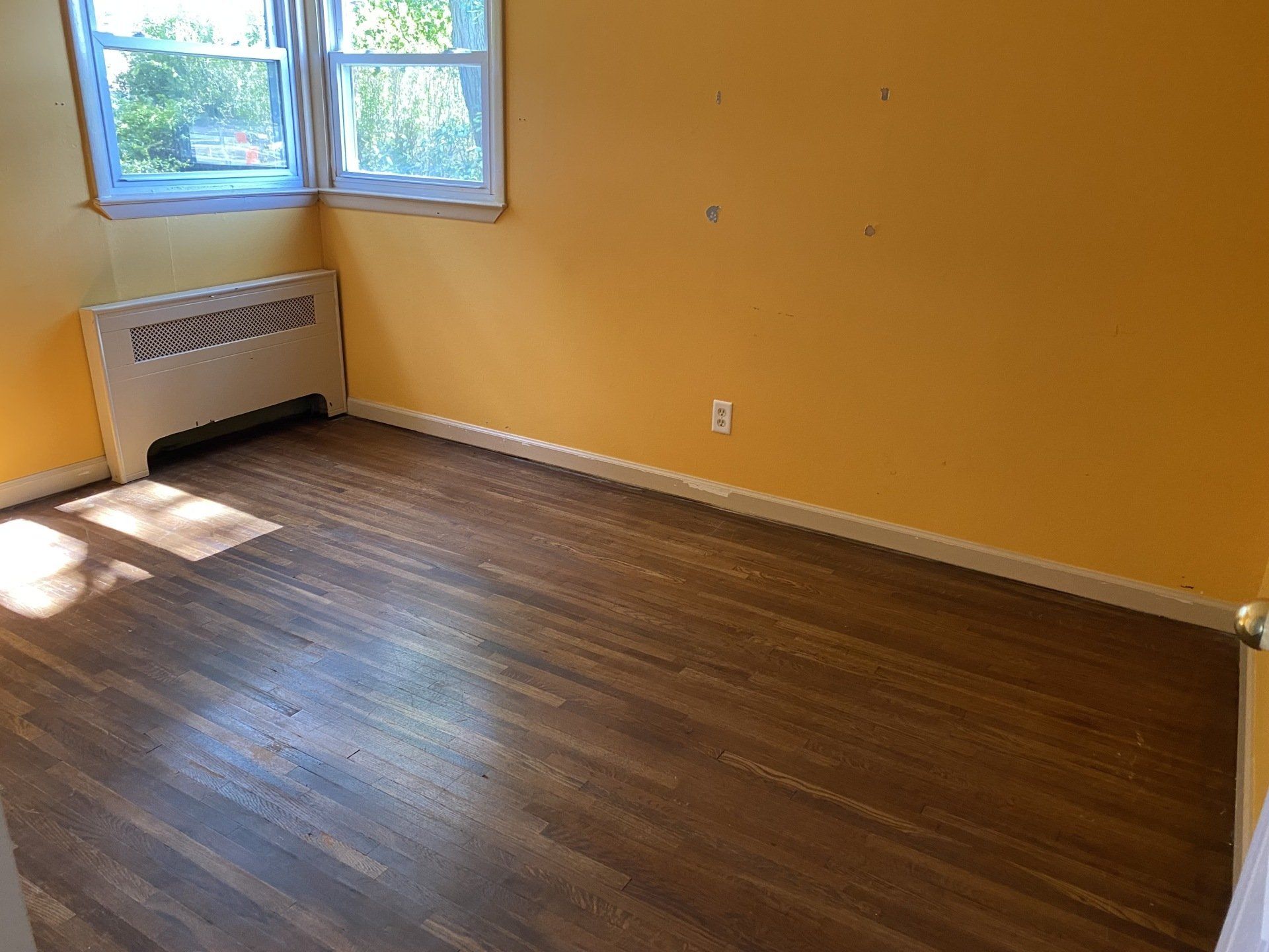 Empty room with yellow walls, wood floor, window and heater.