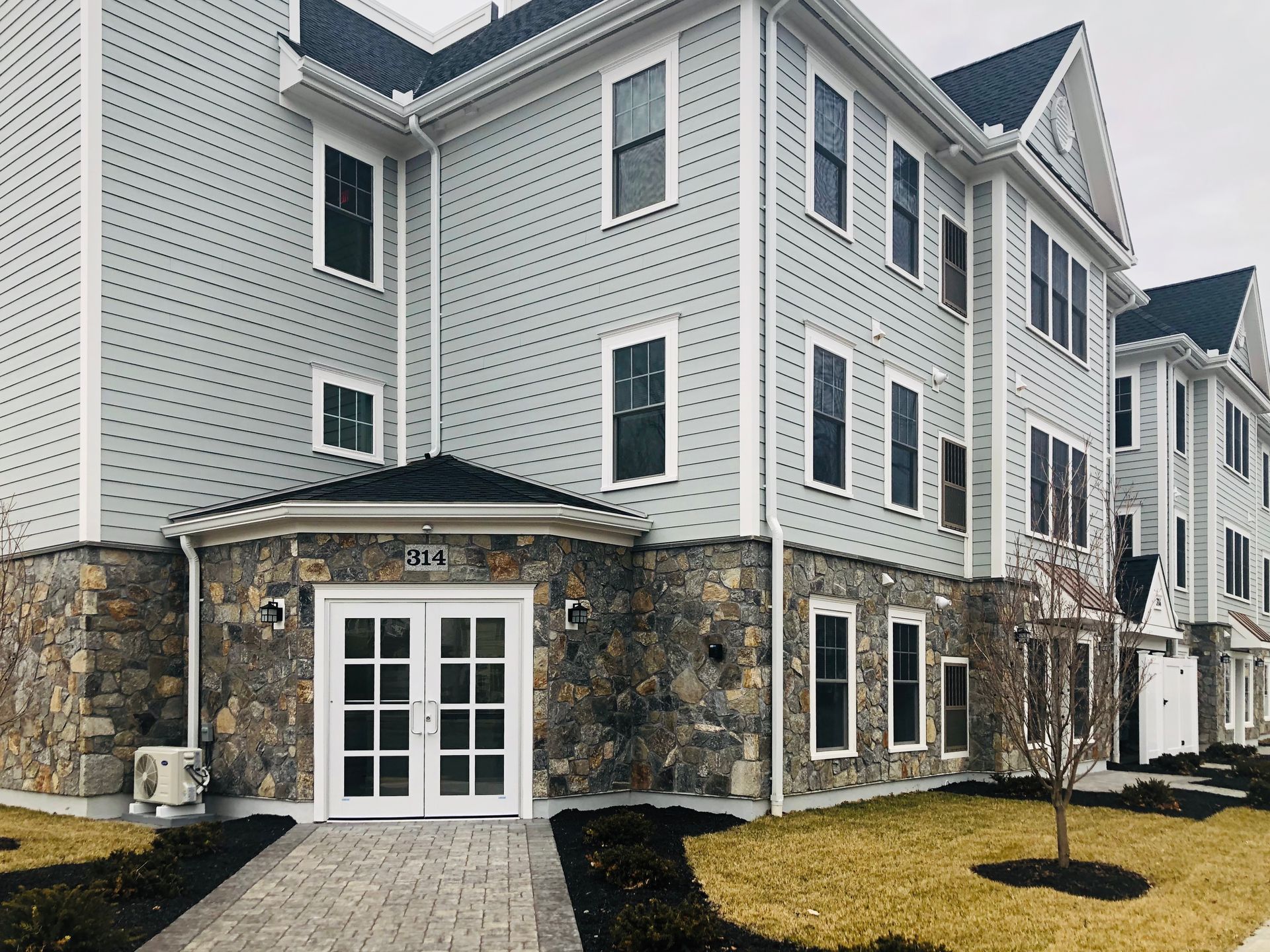 Multi-story apartment building with stone facade entrance, gray siding, and windows.