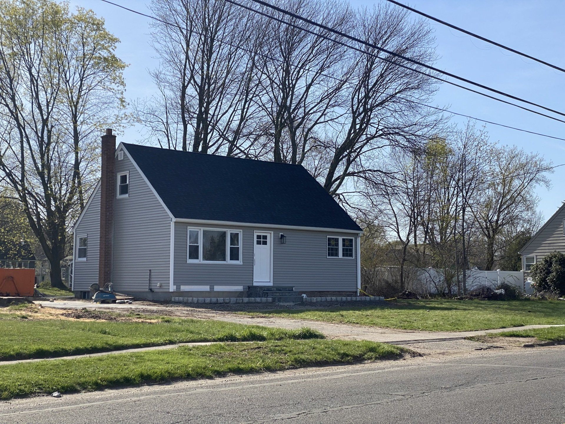 Gray house with dark roof, small front porch, and chimney, trees in background.