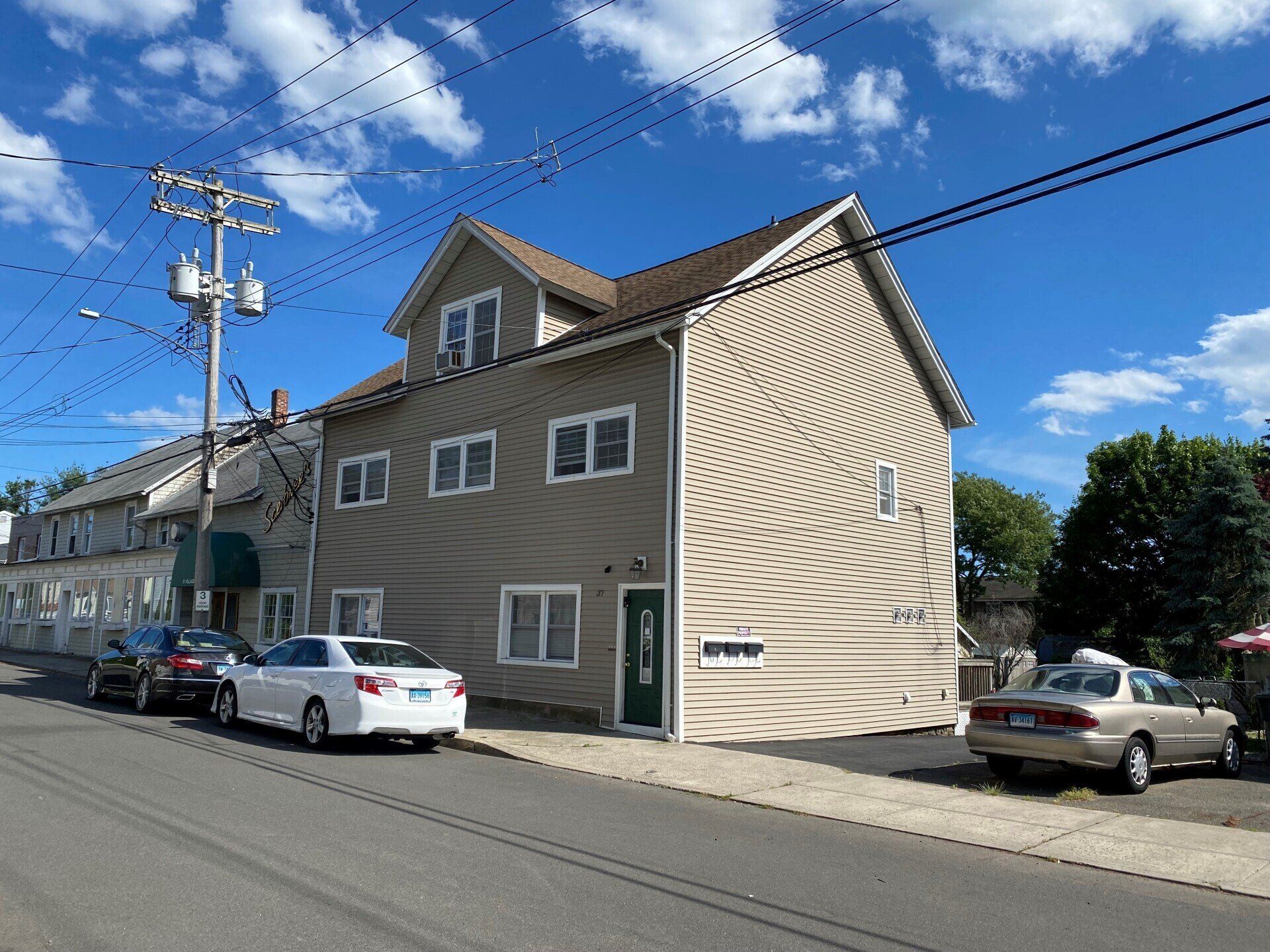 Tan three-story building with swirl design, cars parked on street, utility pole, clear blue sky.