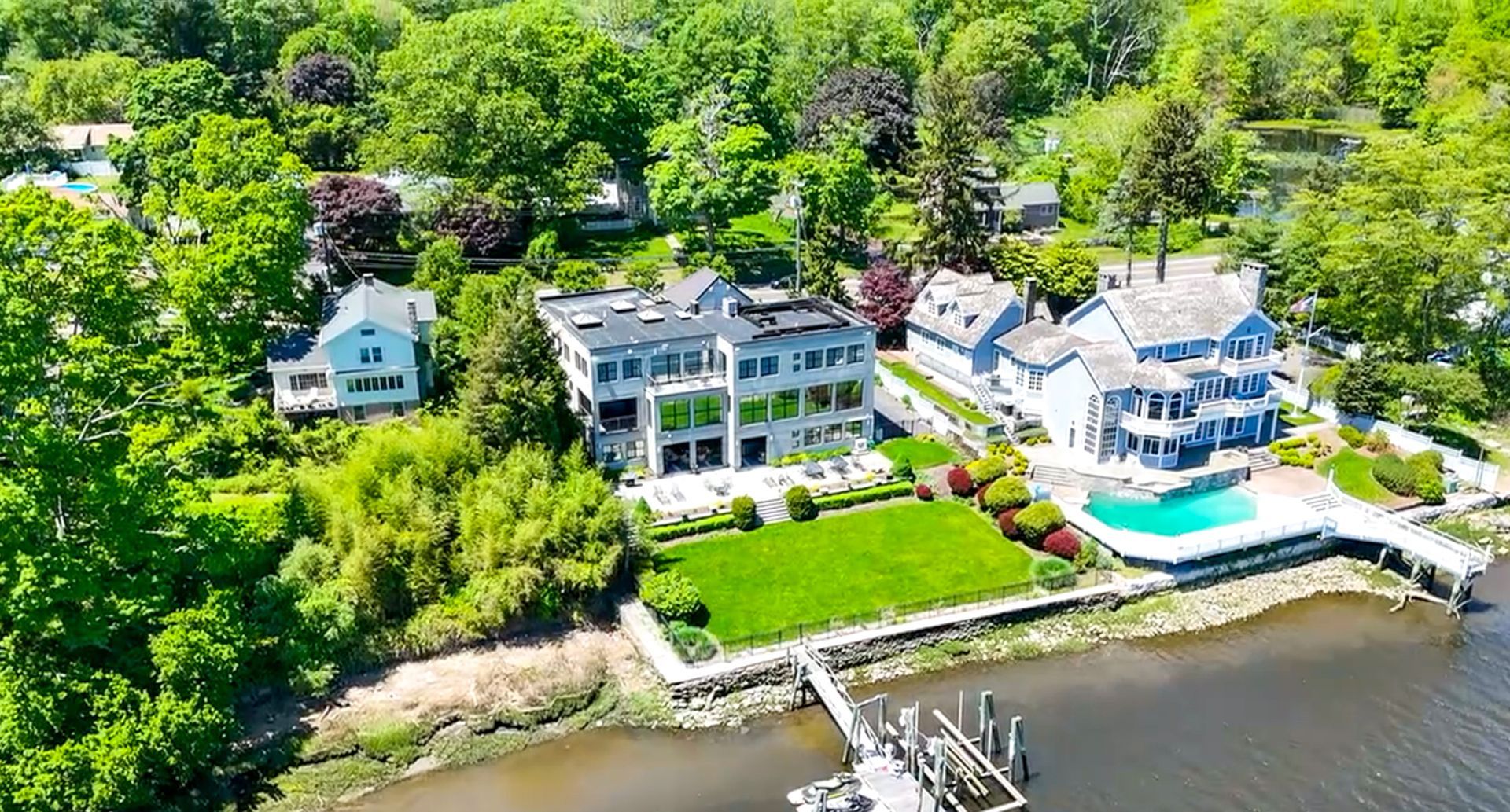 Aerial view of three waterfront houses with pools and docks surrounded by lush greenery.