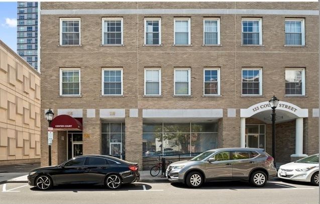 Three-story brick building with windows and entryways, street parking, and cars.
