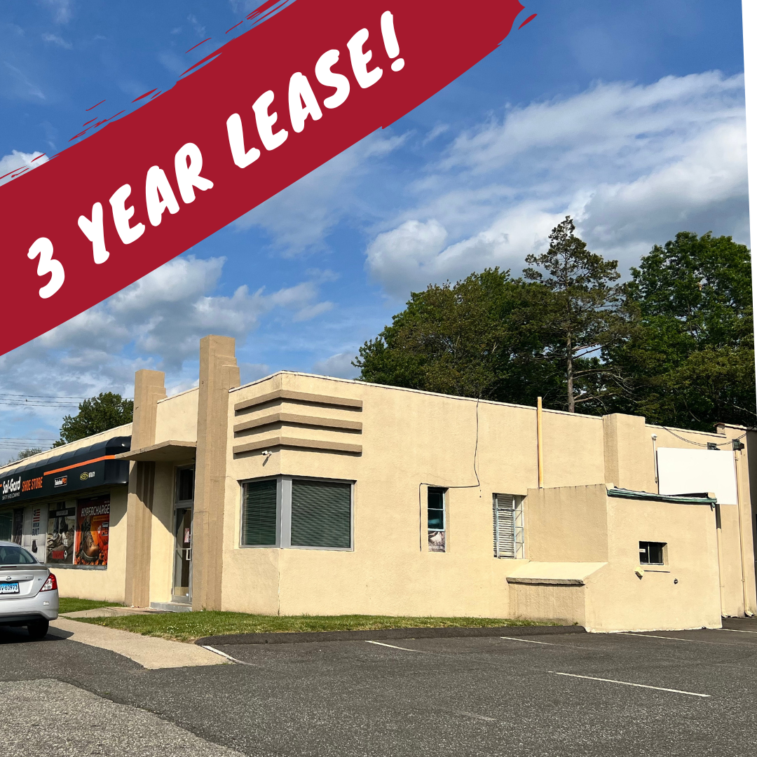 Building with tan stucco and geometric design, for lease. Red banner states 