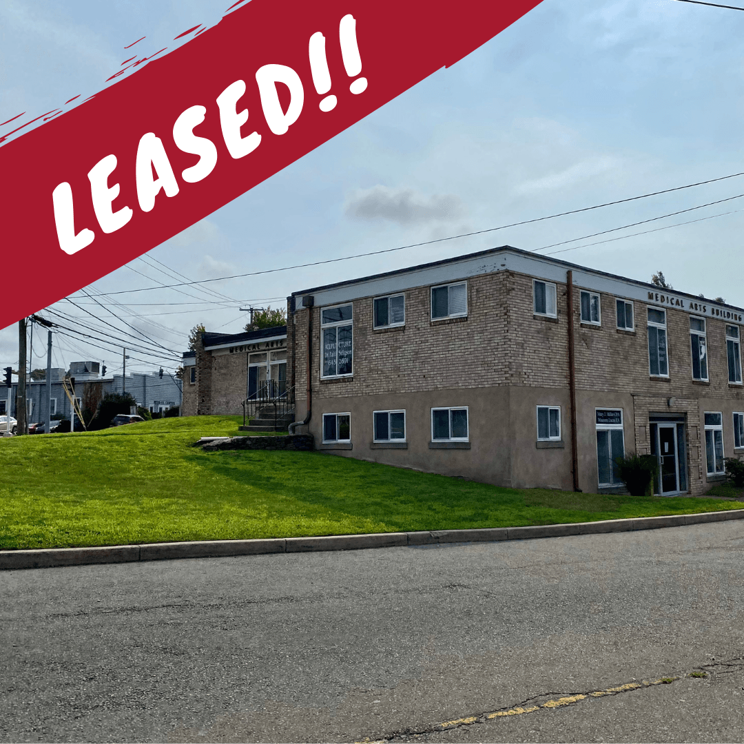 Exterior of a commercial building, grassy area, LEASED! text overlay in red, blue sky.