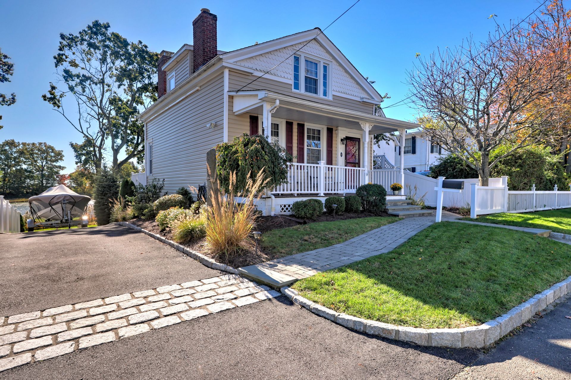 White house with a small porch and manicured lawn, driveway, and a clear blue sky.