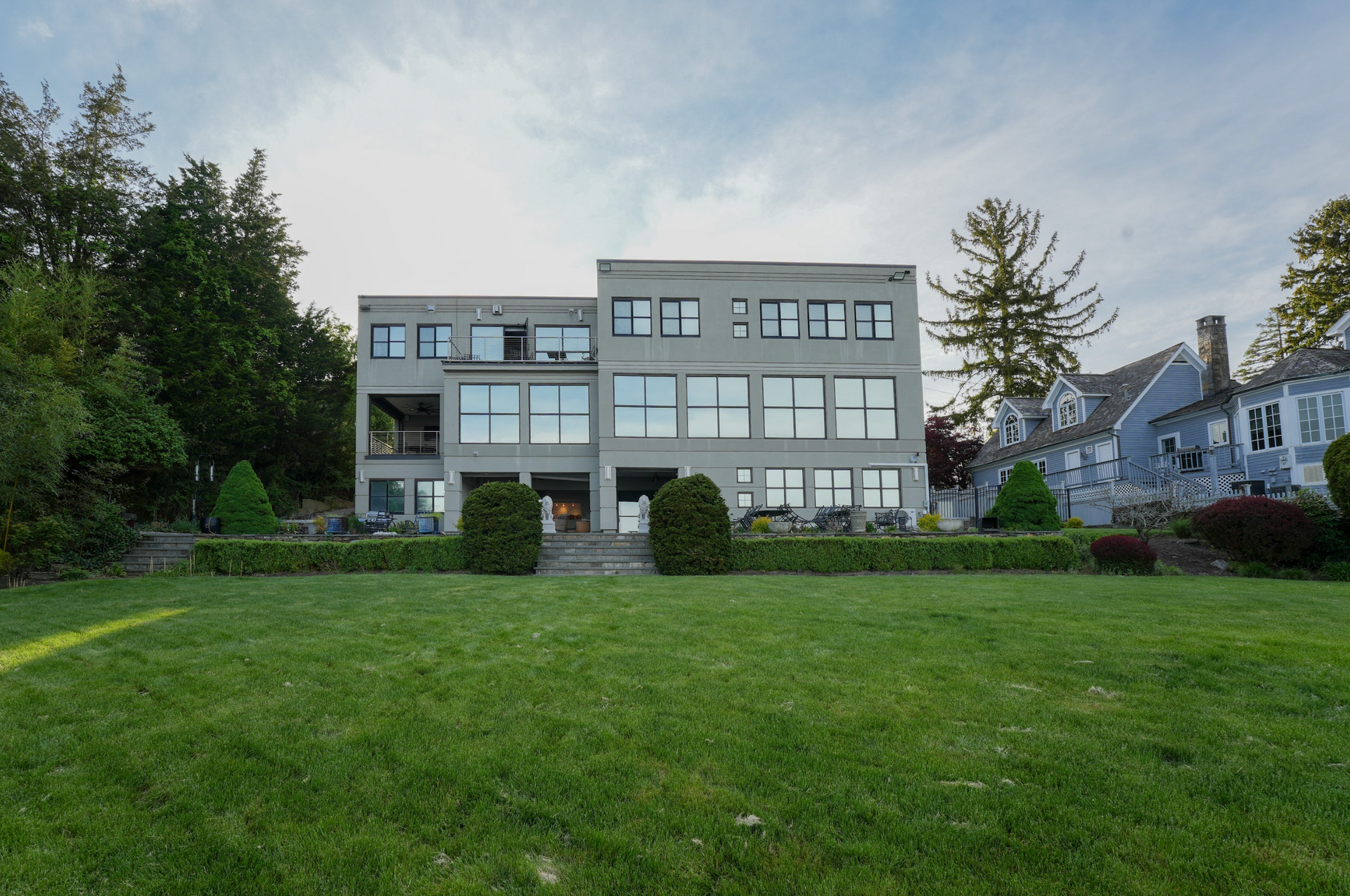 Modern multi-story gray house with large windows and lawn.