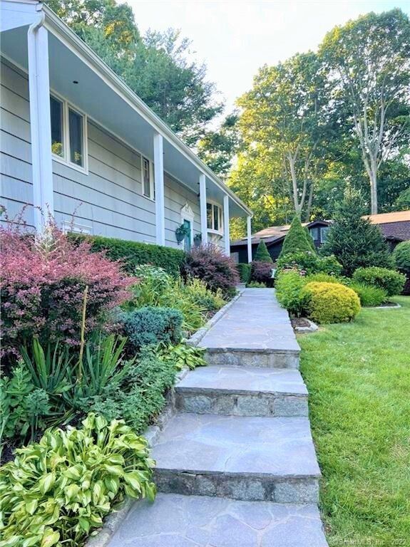 Stone pathway leading up to a light gray house with landscaped garden and green lawn.