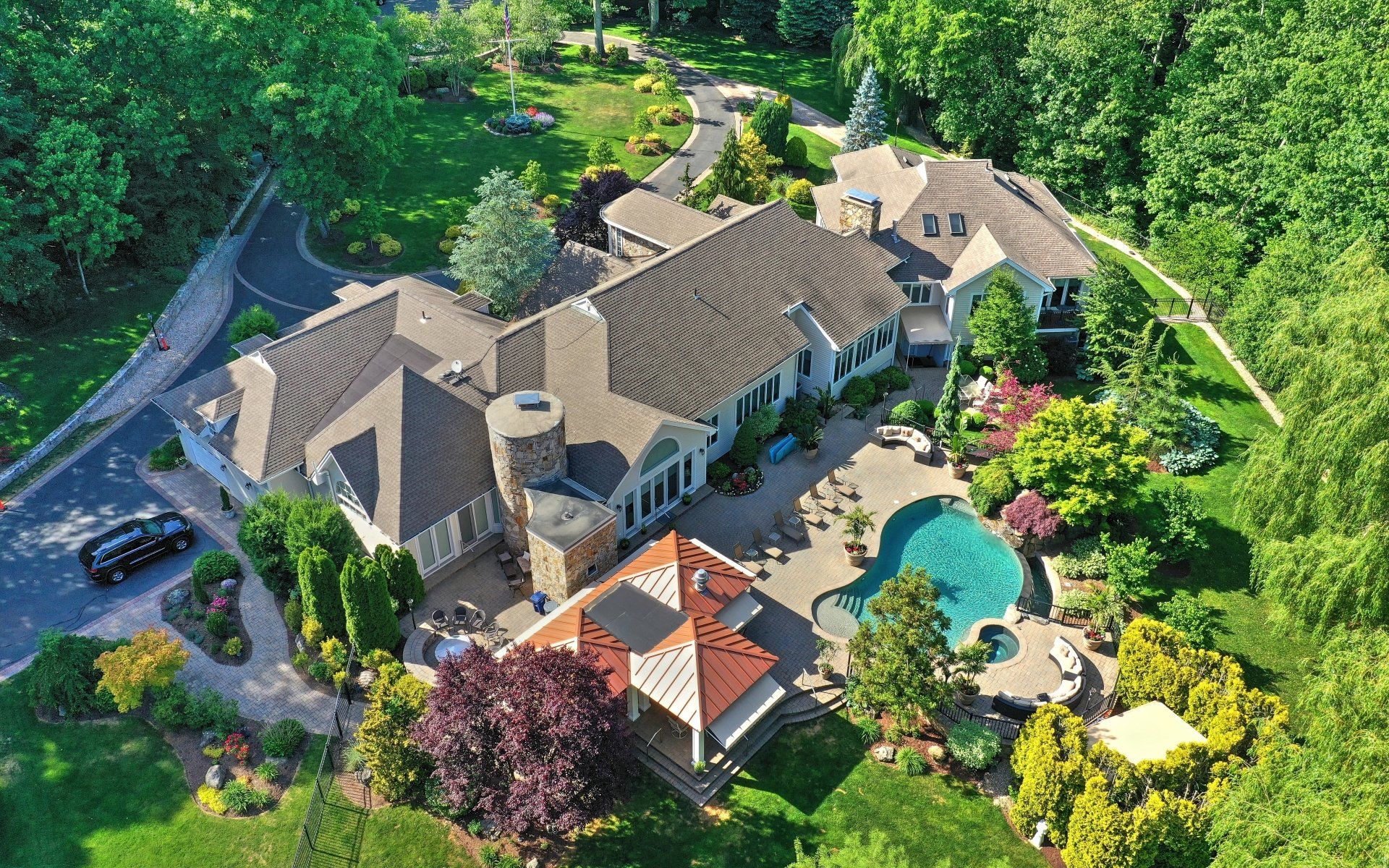Aerial view of a large luxury house with a pool, gazebo, and landscaped gardens surrounded by trees.