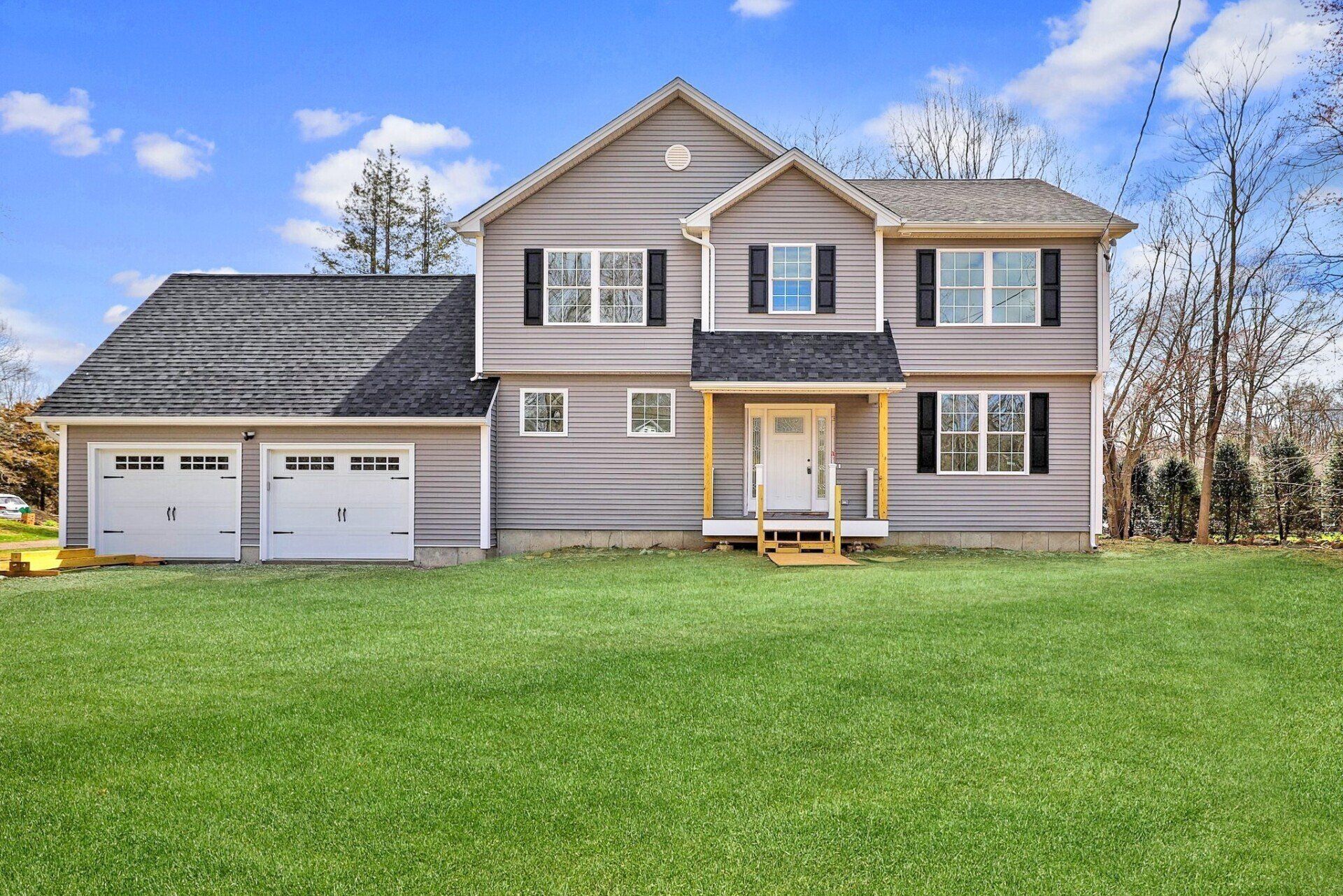 Two-story house with attached garage, gray siding, white trim, green lawn, blue sky.