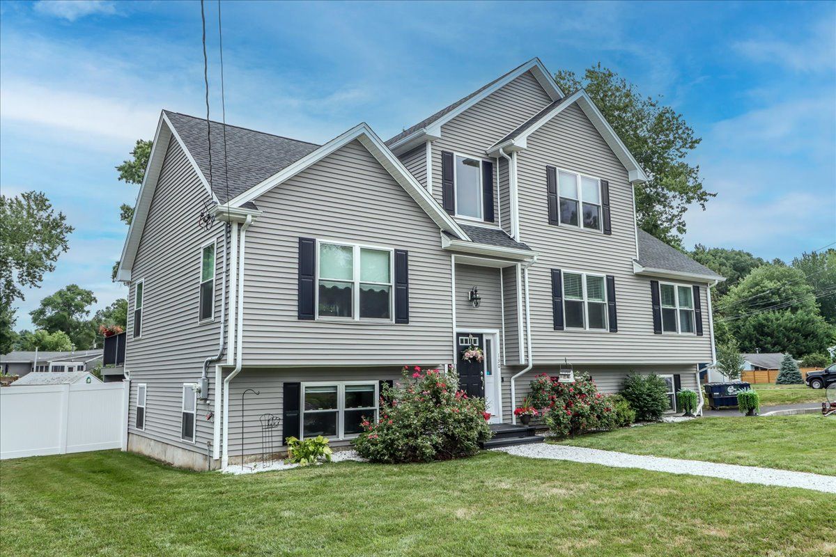 Gray house with black shutters, on a slight hill, with a green lawn and white fence.